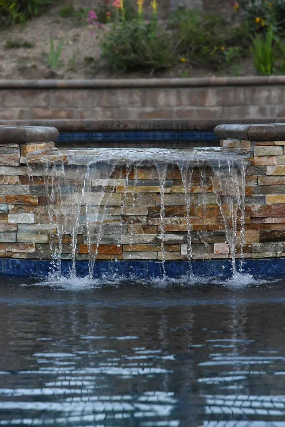 Close-up of a wide sheet of water falling over the stone-faced spa wall into the pool.