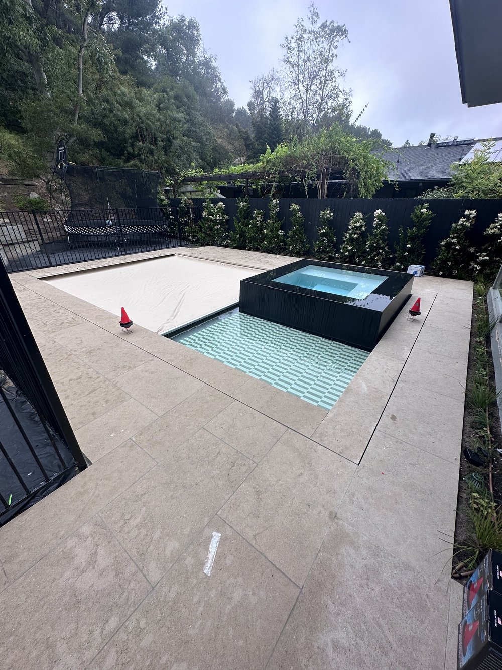 A dark square spa rises beside a pale tiled shallow area and a partially covered rectangular pool.