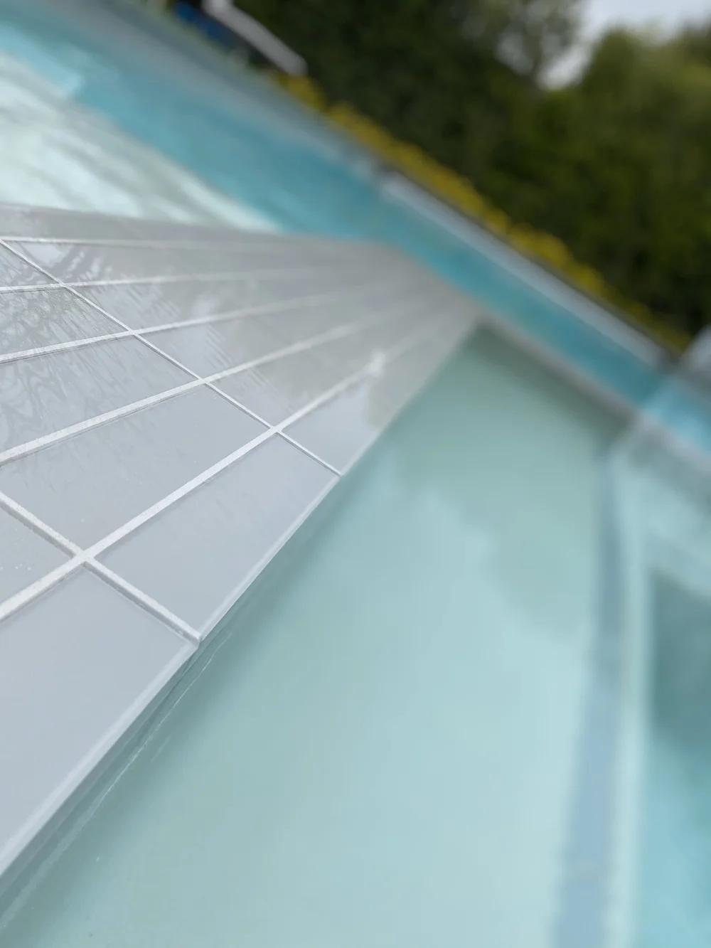 Shallow-focus view along a gray-tiled spa divider beside clear pale-blue water.