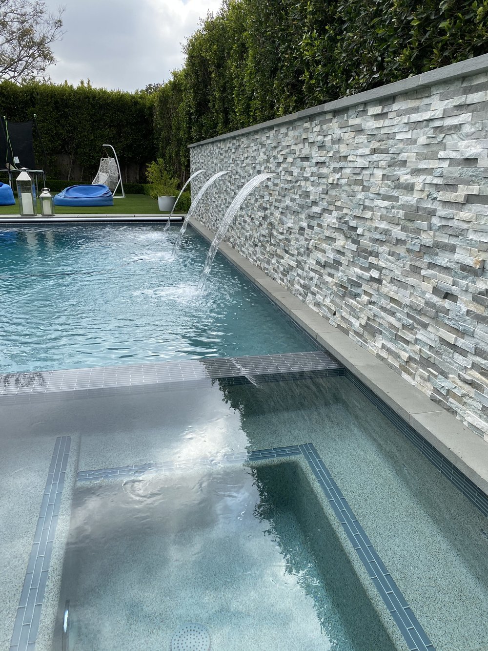 Close view along a bubbling spa and rectangular pool toward arching streams in a textured feature wall.