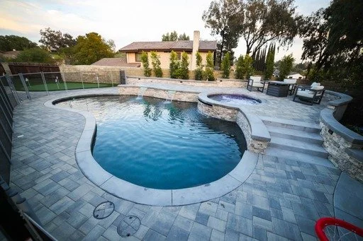 A freeform pool curves around a raised round spa, with broad steps leading to a paved seating terrace.