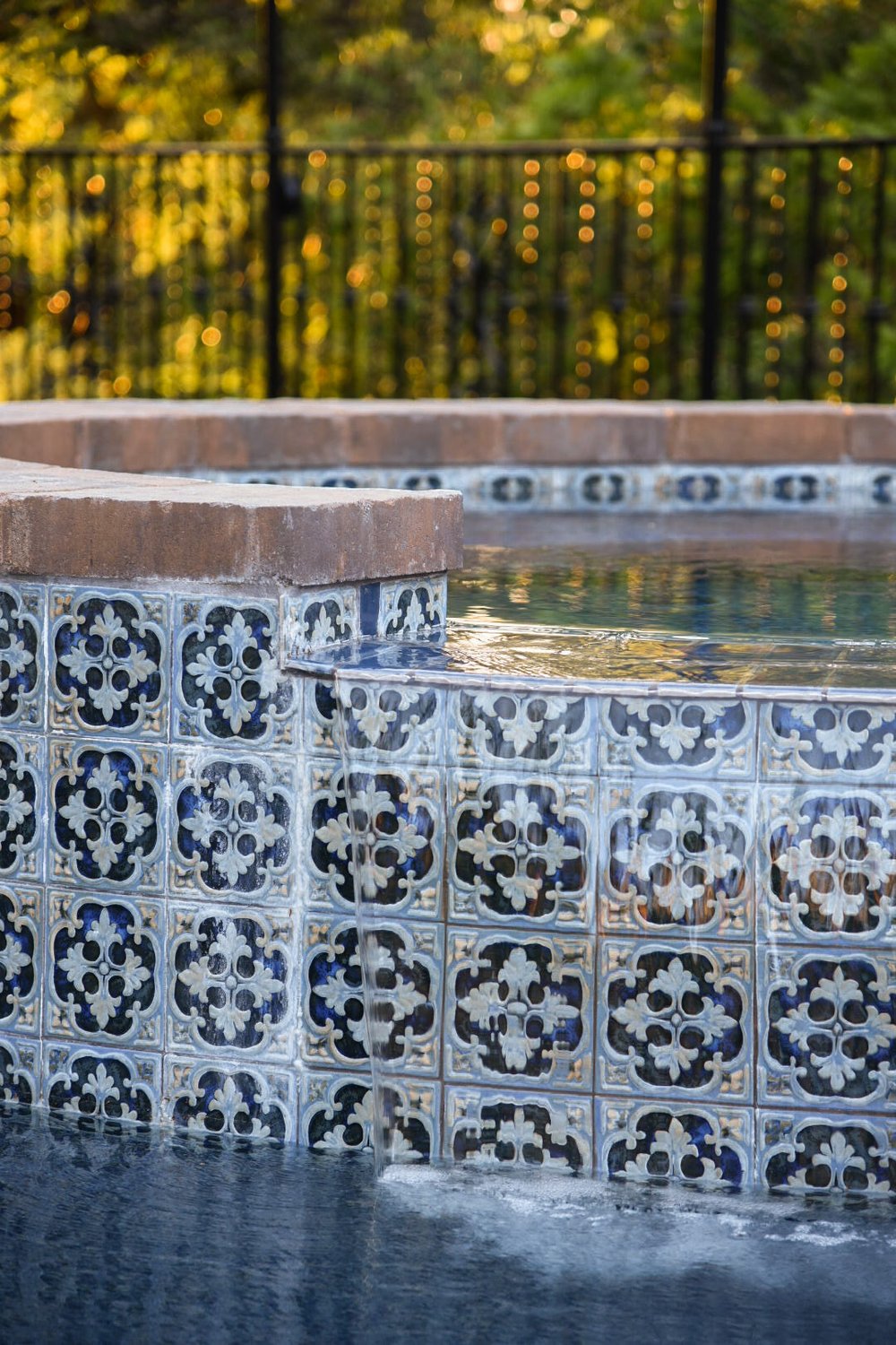 Close-up of a raised spa's blue-and-white patterned tile and water spilling into the pool below.
