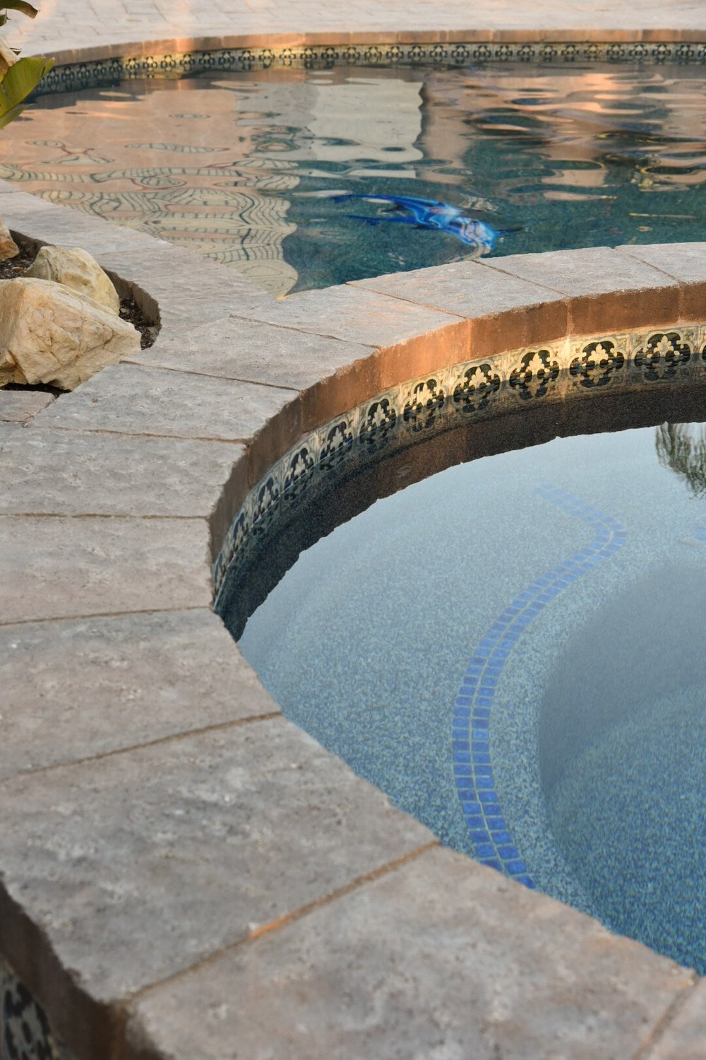 Close view of curved stone coping separating the spa and pool, with waterline tile and submerged seating visible.