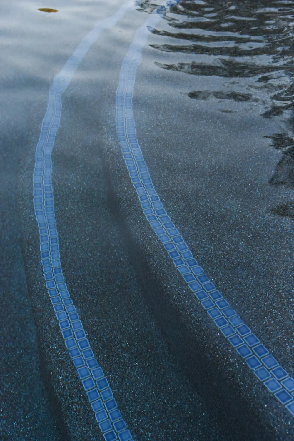 Close-up of curved submerged pool steps outlined with narrow blue mosaic tile bands.