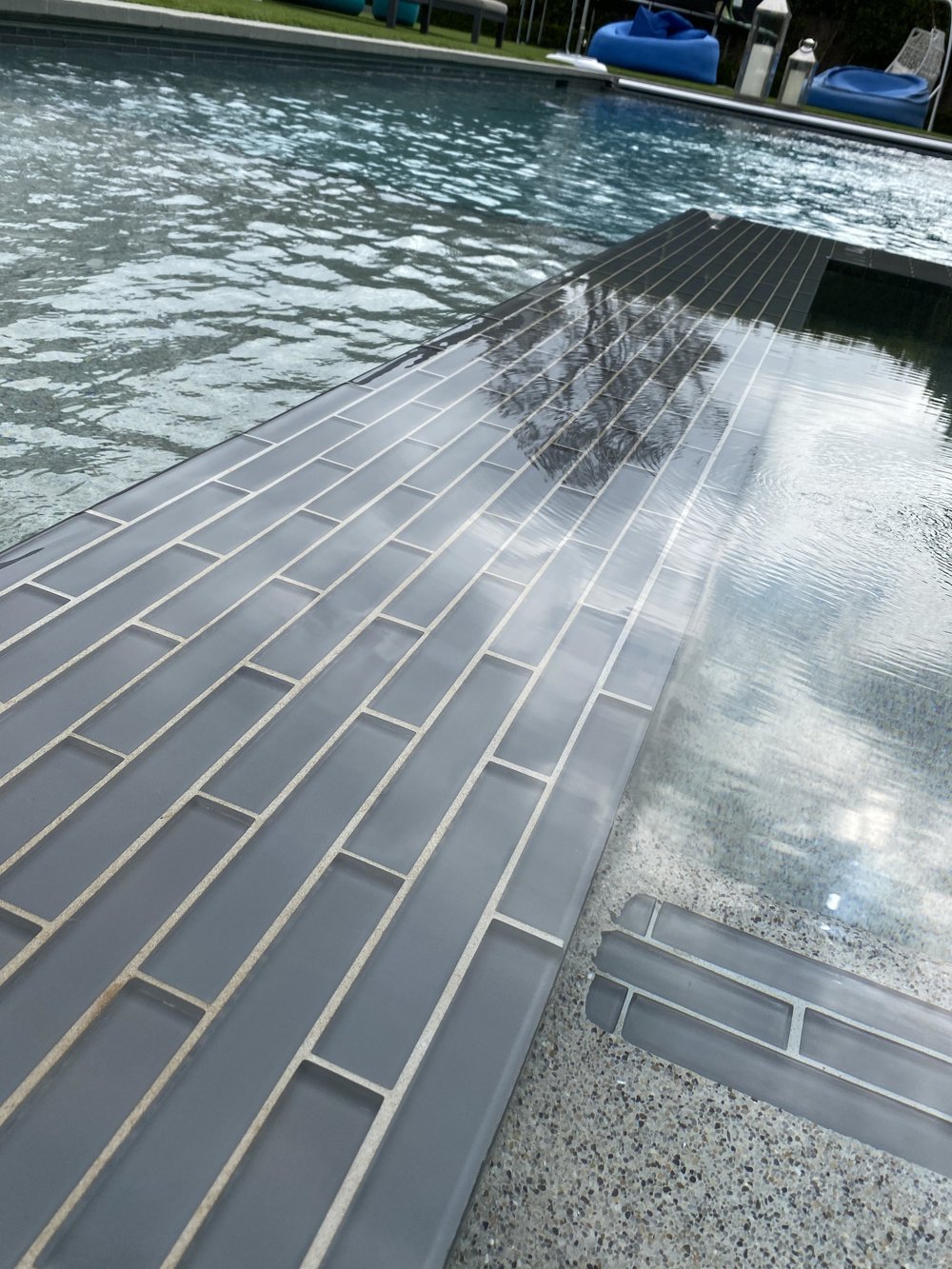 Water ripples over a long gray-tiled spa edge beside bubbling water and a textured interior finish.