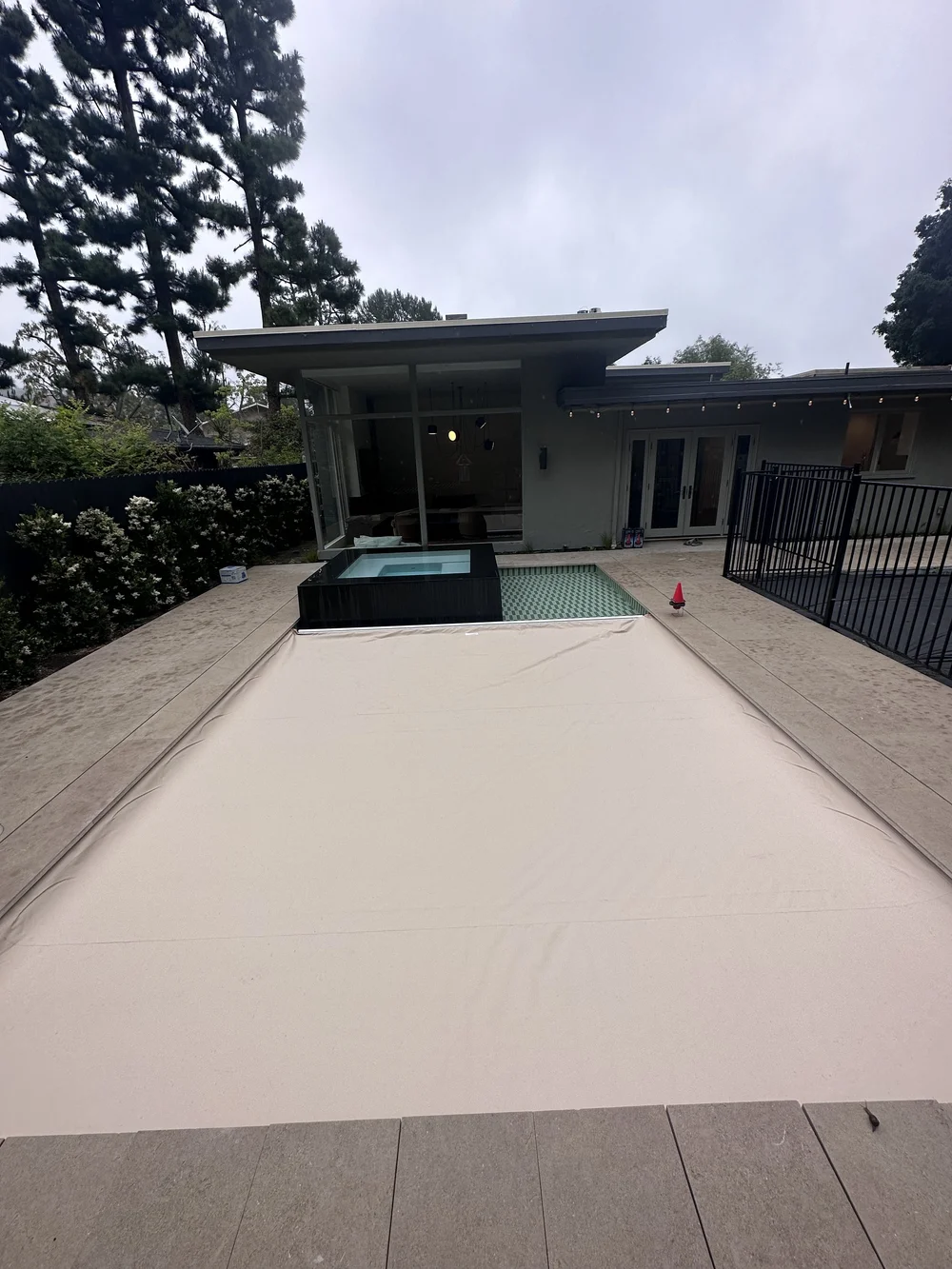 A pale cover spans a long rectangular pool beside a raised dark square spa and a covered patio.