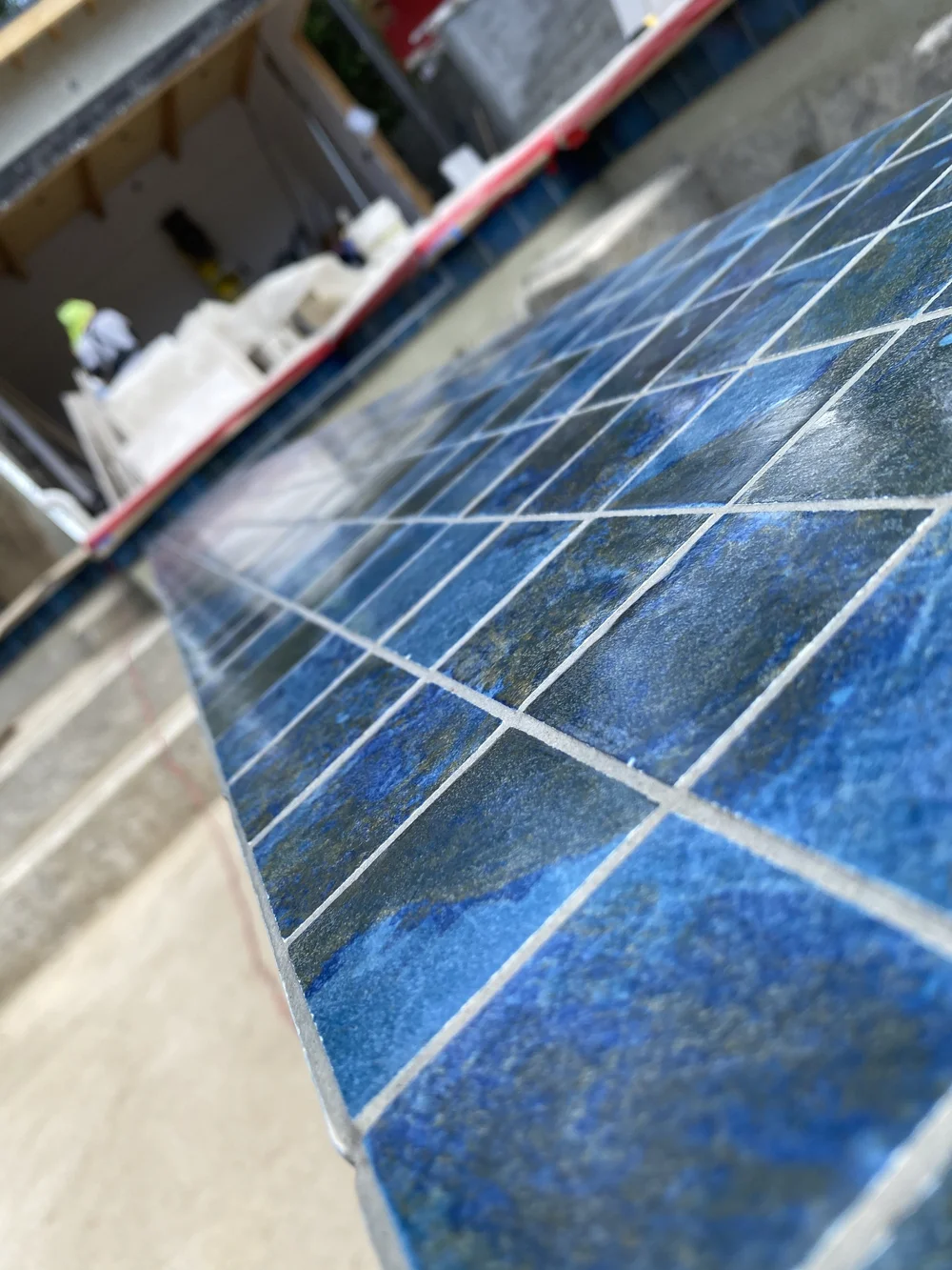 Angled close-up of glossy mottled blue square tiles with pale grout lines along a pool edge.