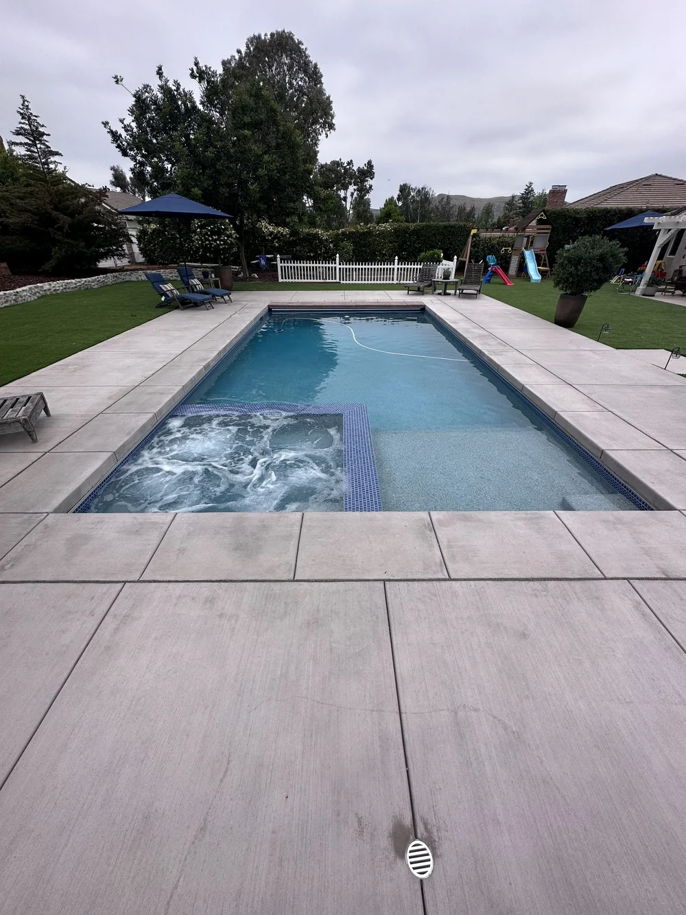 An uncovered rectangular pool has a bubbling square spa and a broad shallow shelf at the near end.