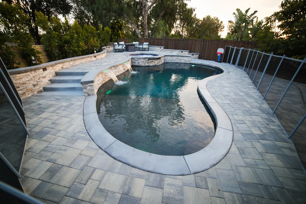 Daytime view of a freeform pool with curved coping, a raised round spa, terrace steps, and a broad paved deck.