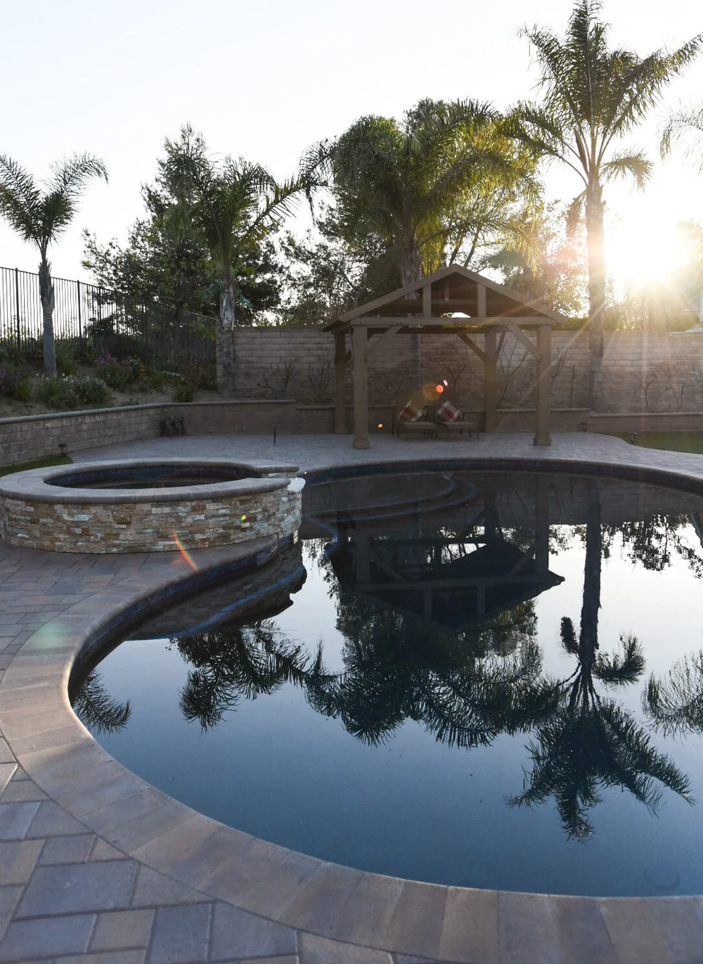 Curved pool and stone-faced round spa beside a paved patio and timber-roofed seating area.