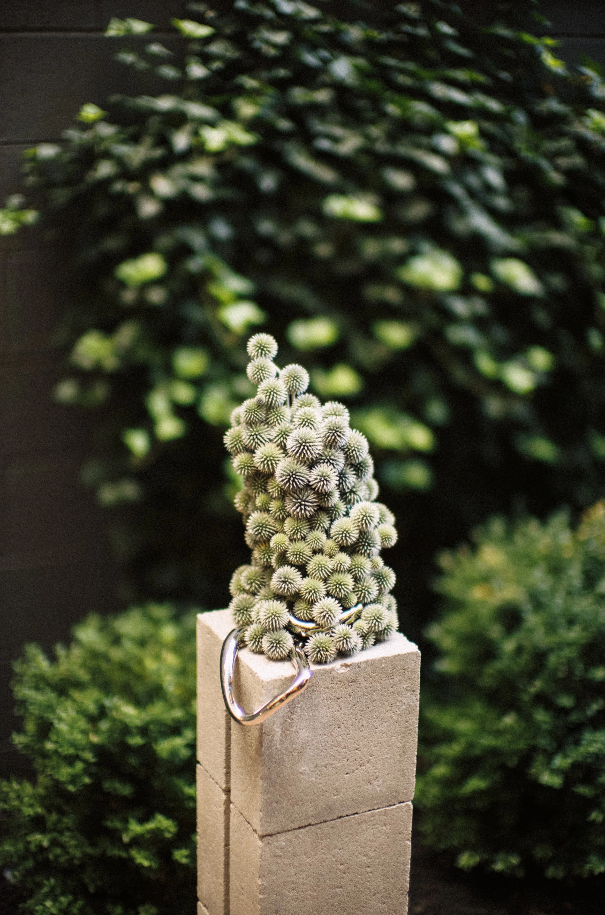 Floral sculpture on cinderblock column. Made of textural, green spheres of thistle with polished chrome interwoven through it.