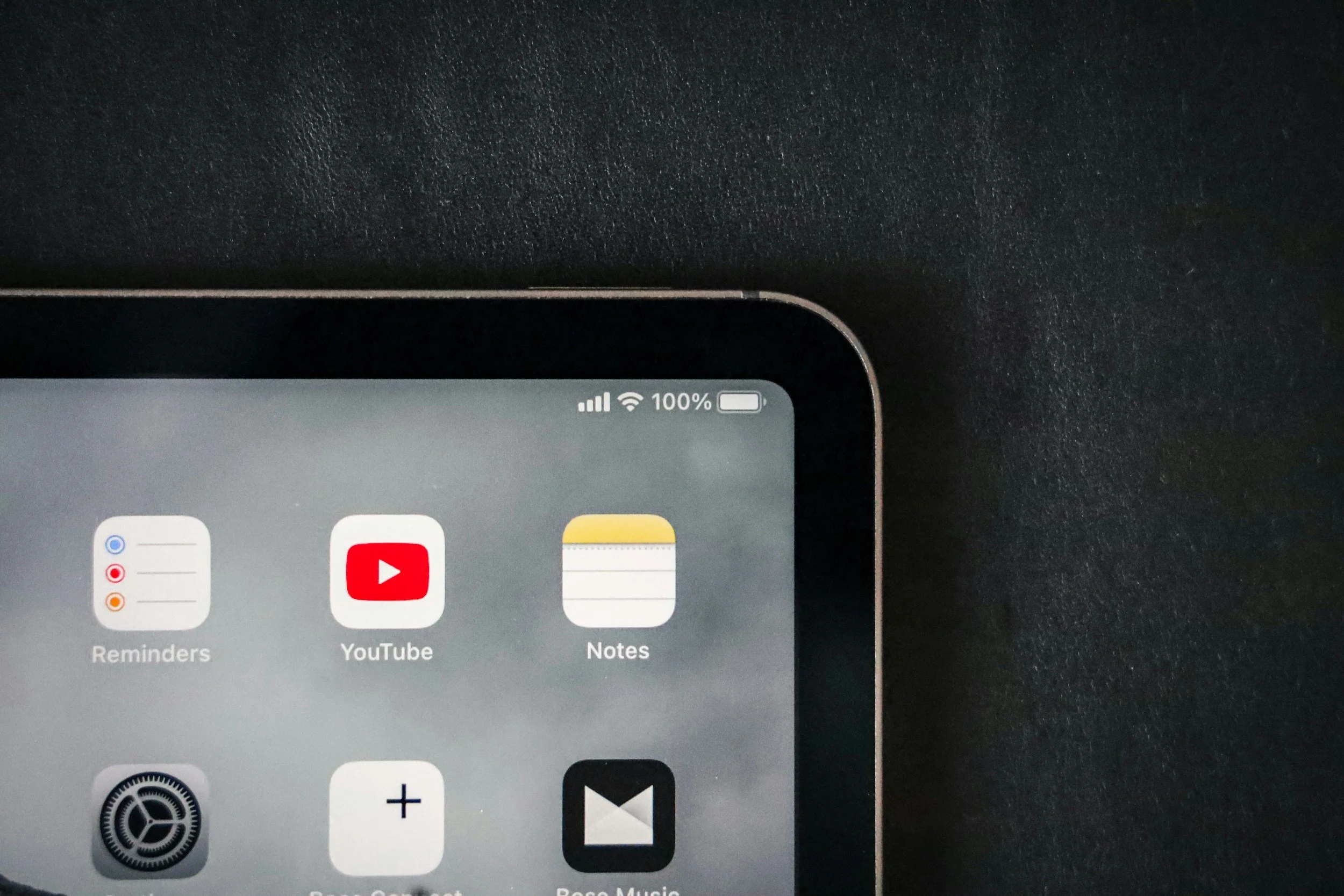 Part of a smartphone screen showing app icons for Reminders, YouTube, Notes, and Settings, with the battery, Wi-Fi signals, and 100% battery indicator at the top right corner.