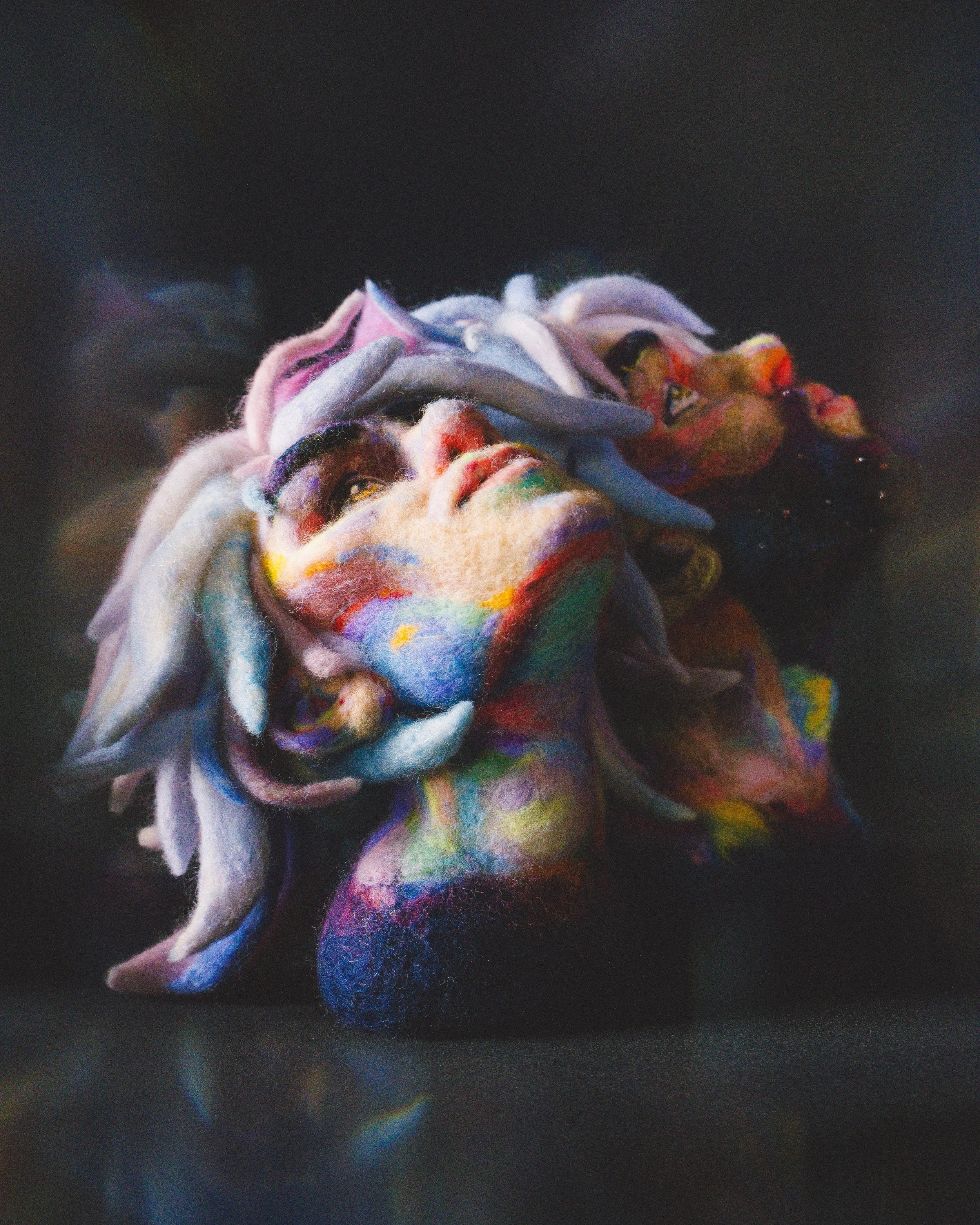 Fanart: Close-up of a multicolored felted wool sculpture of Jayce and Viktor from the TV show Arcane, looking up against a dreamy dark background.
