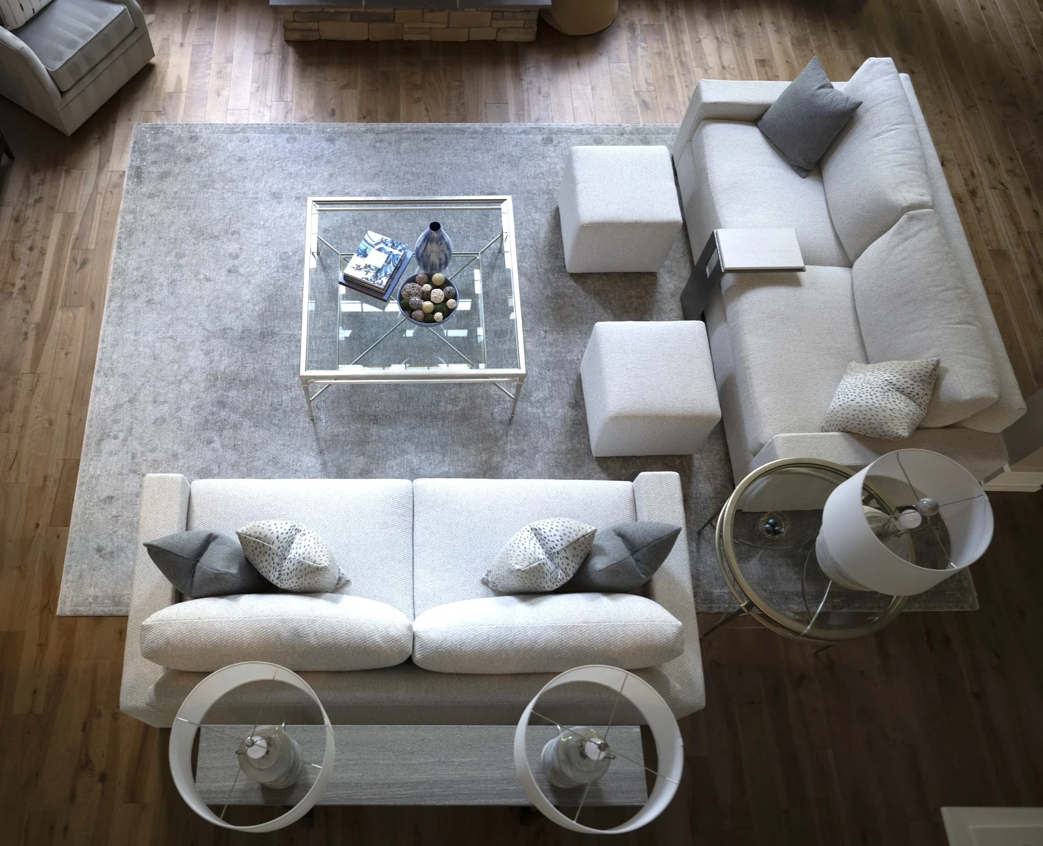 Top-down view of a living room with a large cream-colored sofa, a light gray area rug, a glass-top coffee table with decorative items, and a white chair with a curved back.