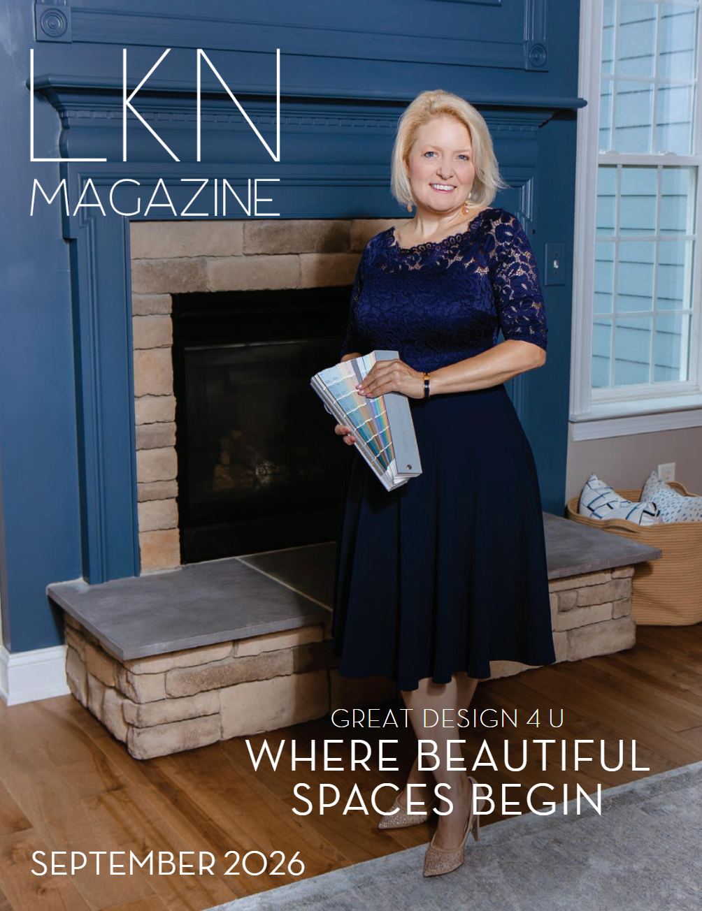 A woman in a navy blue lace top and skirt standing in front of a fireplace holding a color swatch. Text on image reads, 'LKN Magazine, Great Design 4 U, Where Beautiful Spaces Begin, September 2026.'