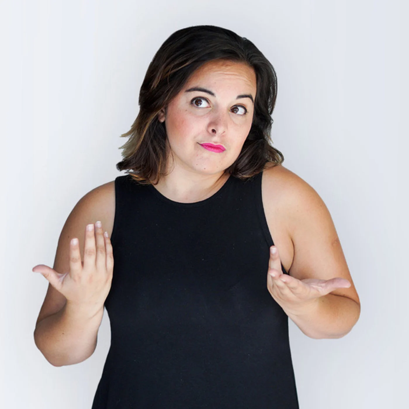 Woman with shoulder-length brown hair wearing a black sleeveless top, making a shrugging gesture with her hands, and looking to her left with a puzzled expression.