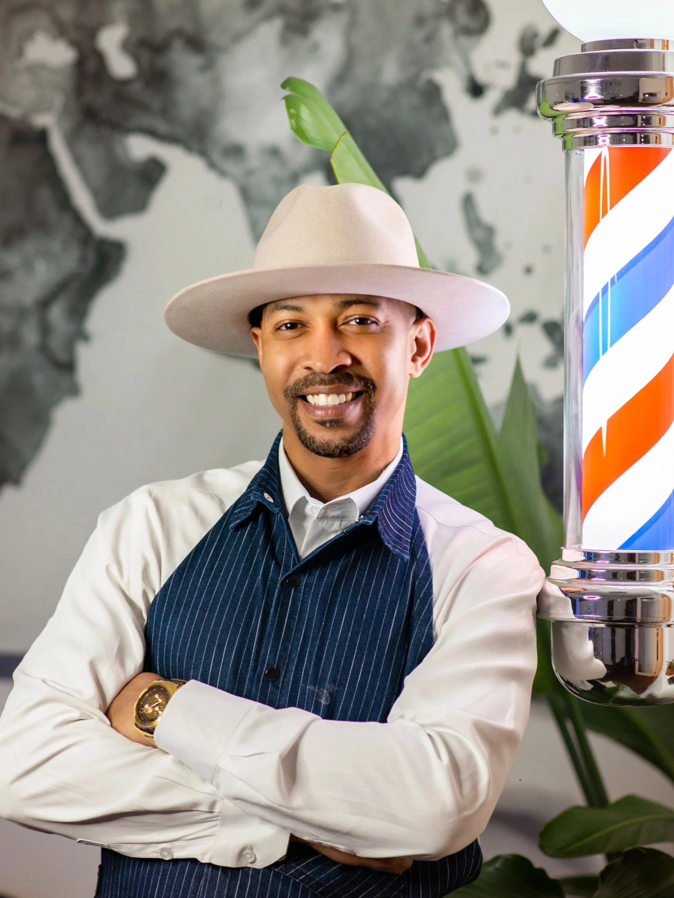 Master Barber Demetrius Kiel stands confidently with arms crossed in front of a barber pole at Groomed by Kiel executive barbershop in Huntsville, AL