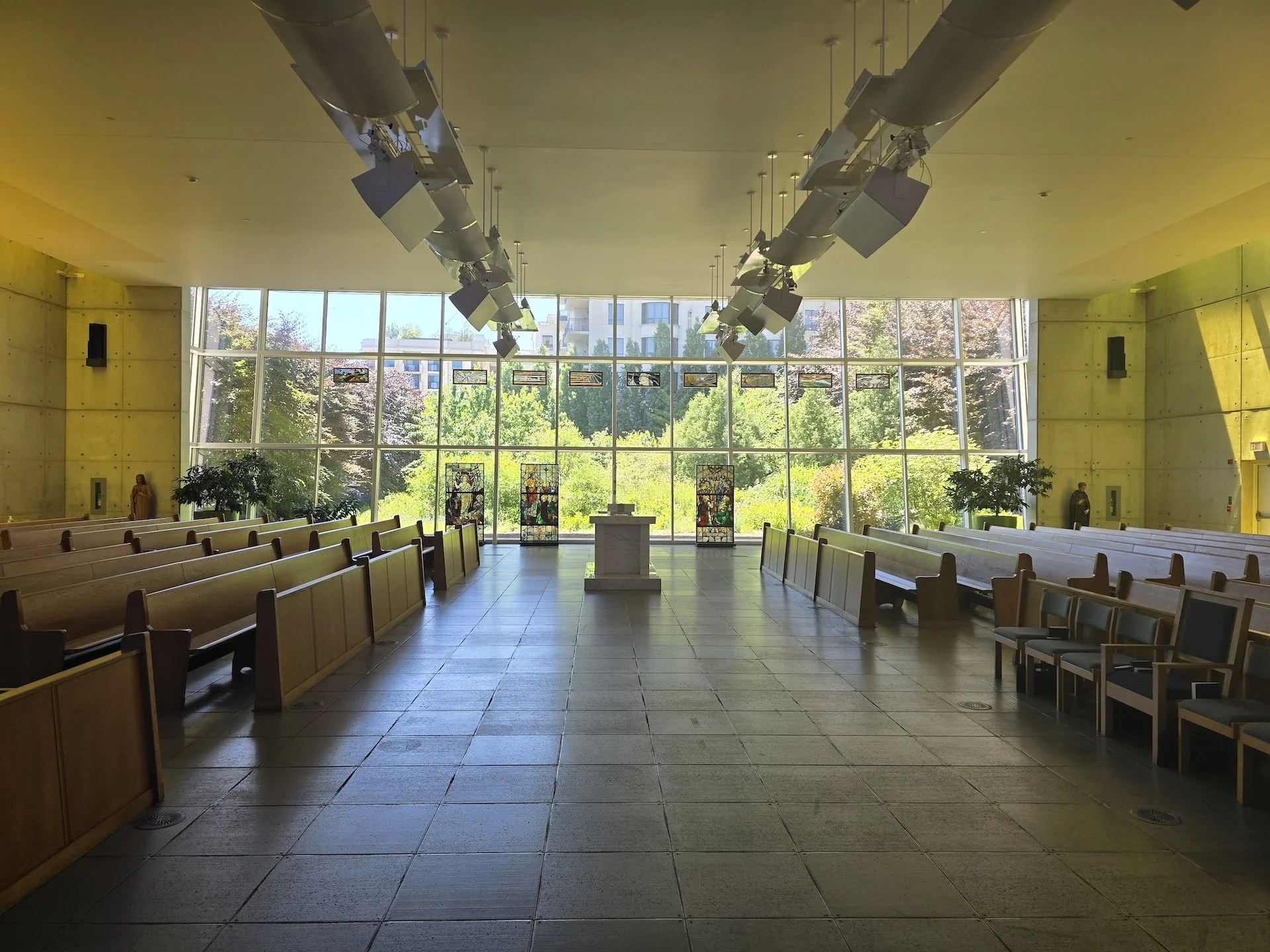 Pews facing one another in St. Gabriel’s Church, with the garden visible beyond the glass wall.