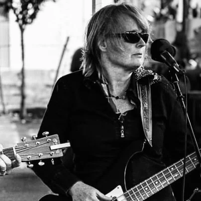 Female rock bass player wearing sunglasses and dark clothing performing at a recent farmer's market in New Jersey.