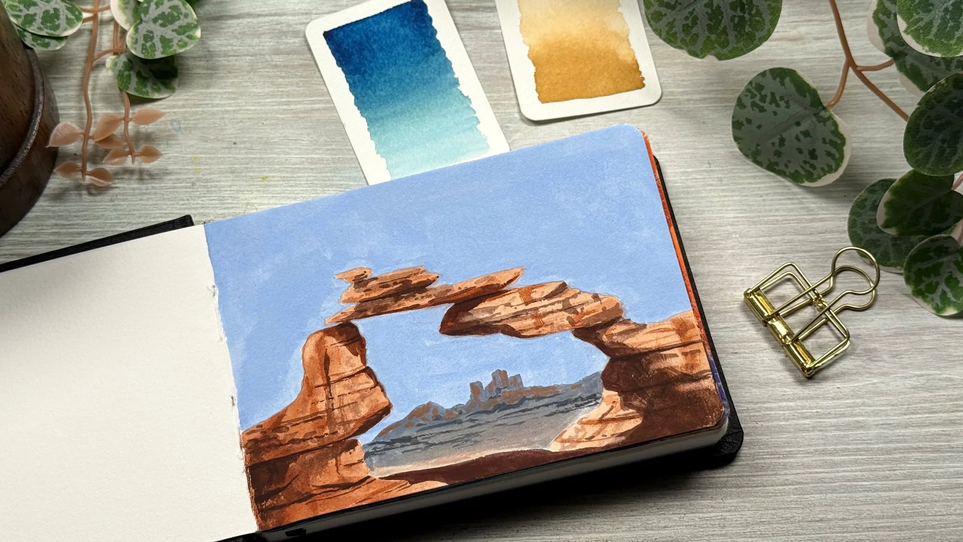 A gouache painting of a red rock arch in the desert.