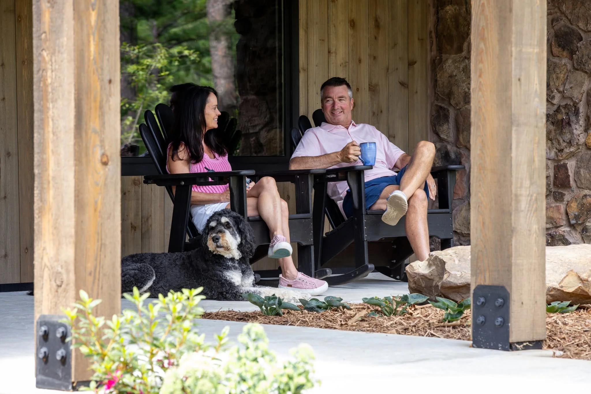 Couple relaxing in rocking chairs with their dog on a porch.