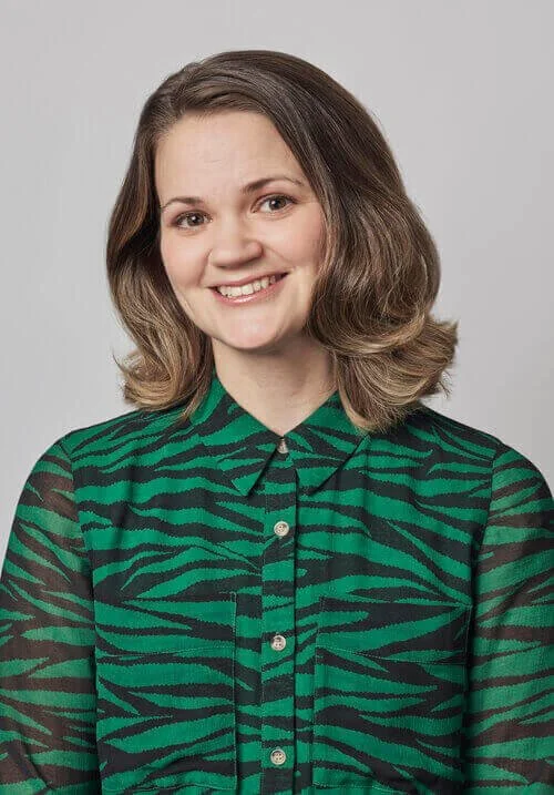 Smiling woman in green and black zebra blouse against light gray background.