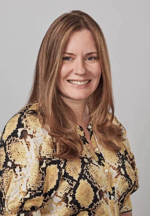 Smiling woman with long light brown hair wearing snakeskin-patterned blouse.