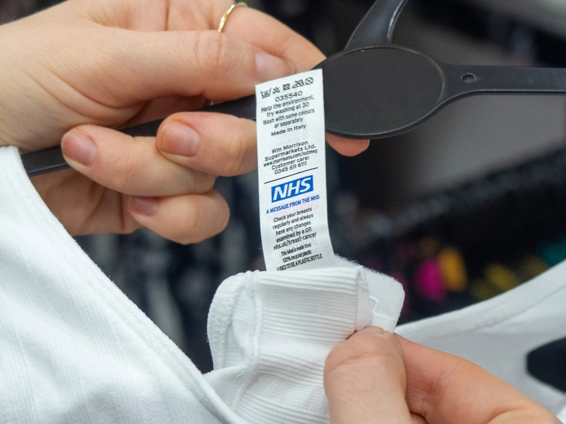 Close-up of hands holding a clothing tag and a strap, with care instructions and NHS logo visible.