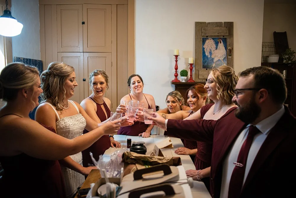 Group of people toasting with drinks, dressed in formal attire, inside a building with wooden cabinets and artwork.
