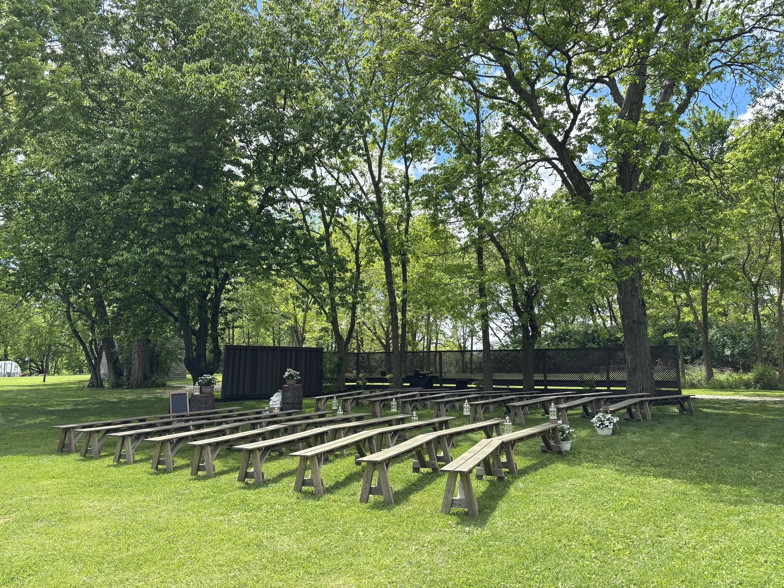 Outdoor wedding ceremony setup with wooden benches, a decorated archway, and trees in the background.