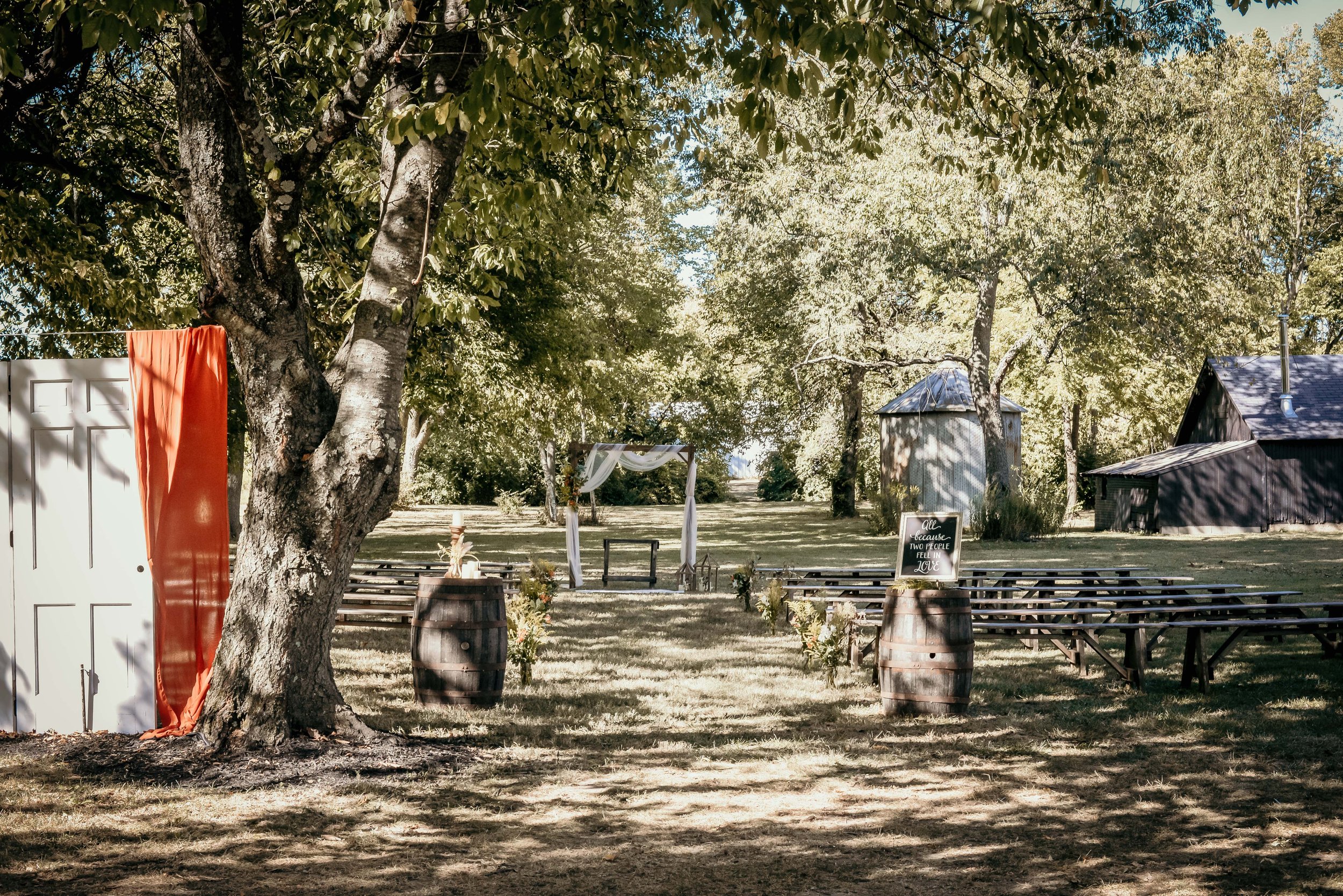 Outdoor wedding ceremony setup with wooden benches, a decorated archway, and trees in the background.