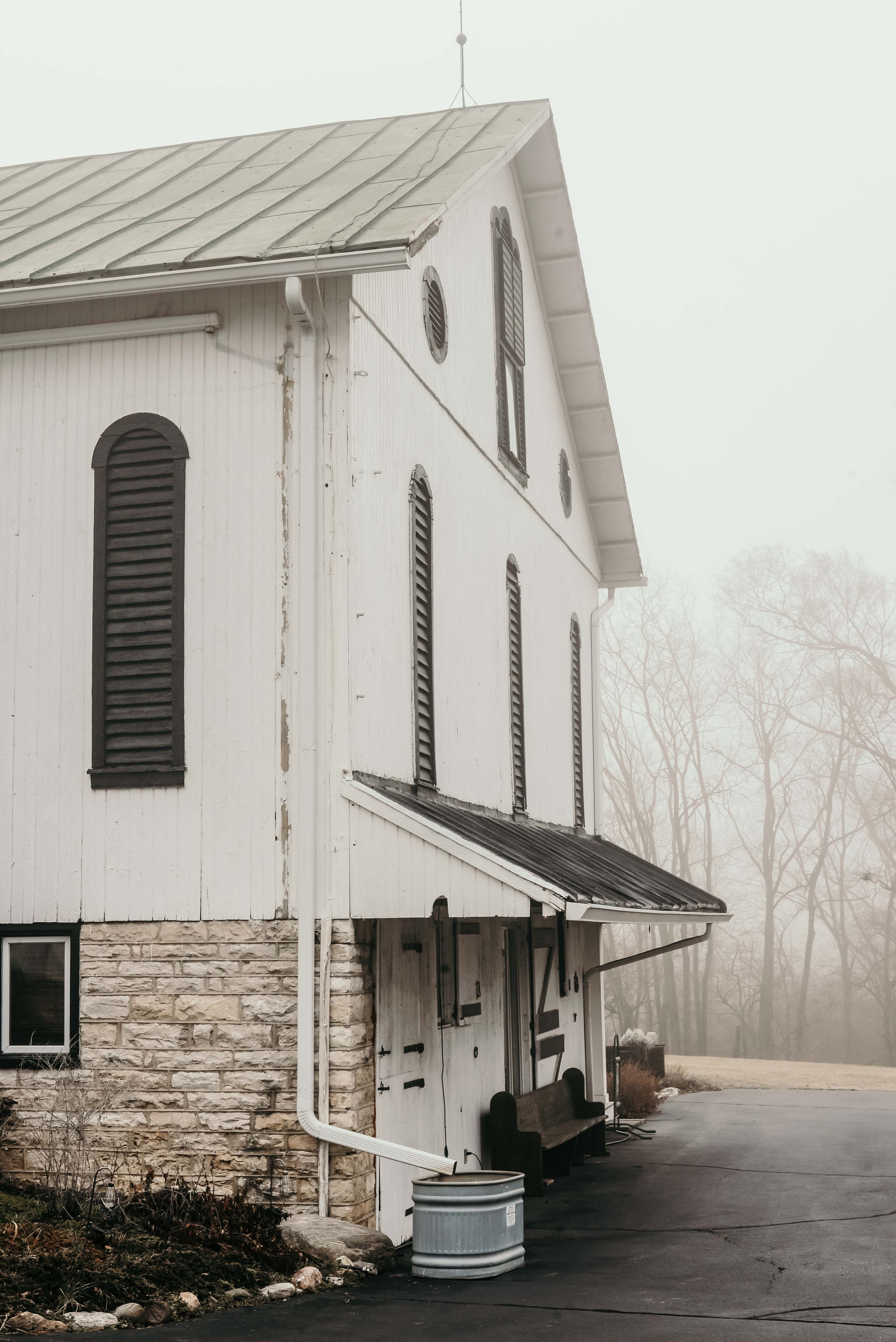 White barn with black shutters and weathered stone foundation, surrounded by fog. The Ohio Barn. Rustic Wedding Venue. Barn Venue. Ohio Wedding Venue. Dayton Ohio