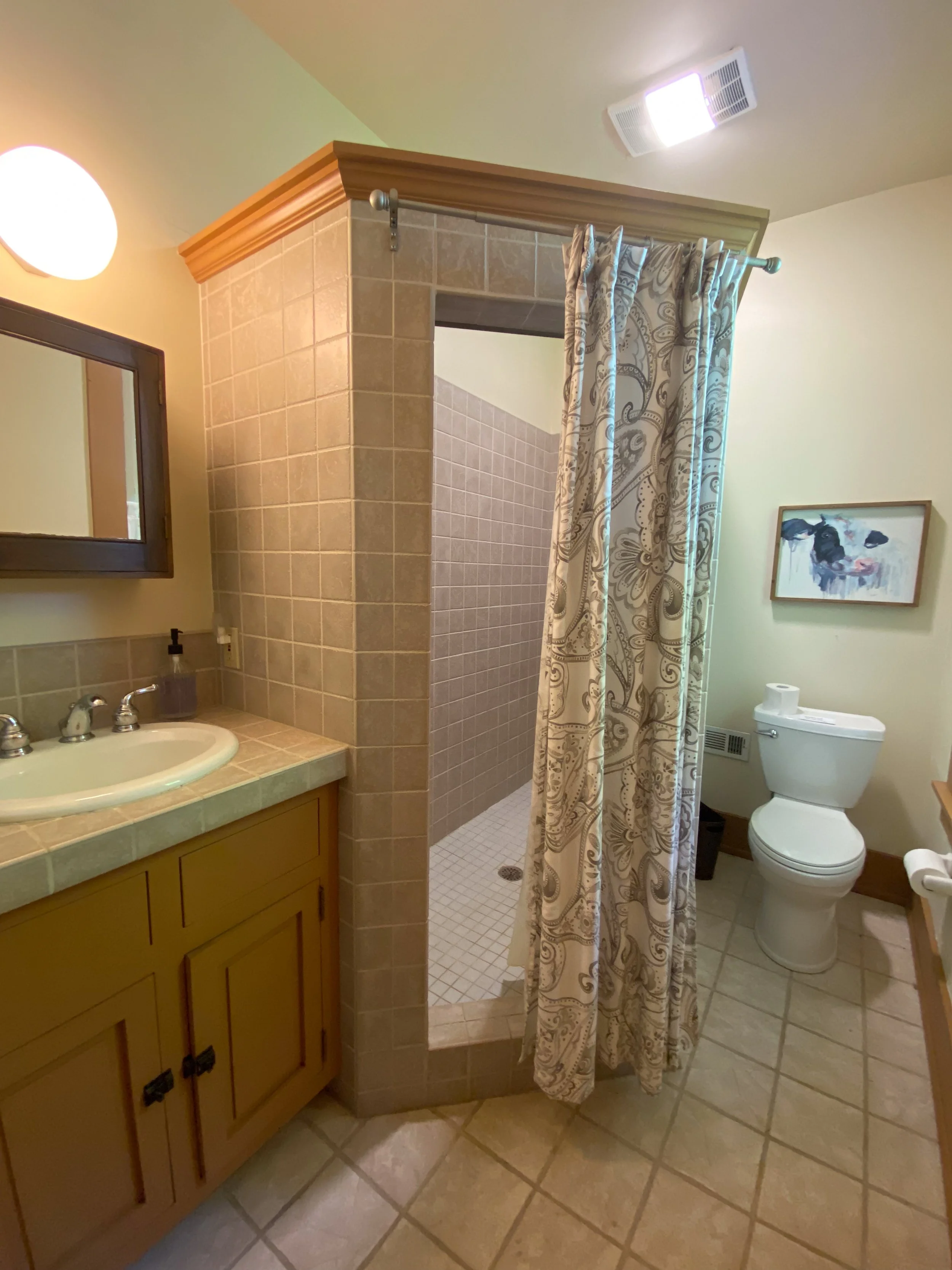 Bathroom with a shower, sink with countertop, toilet, and decorative shower curtain. The Ohio Barn. Fairborn, Ohio. Southern Ohio. Barn Weddings. Venue.