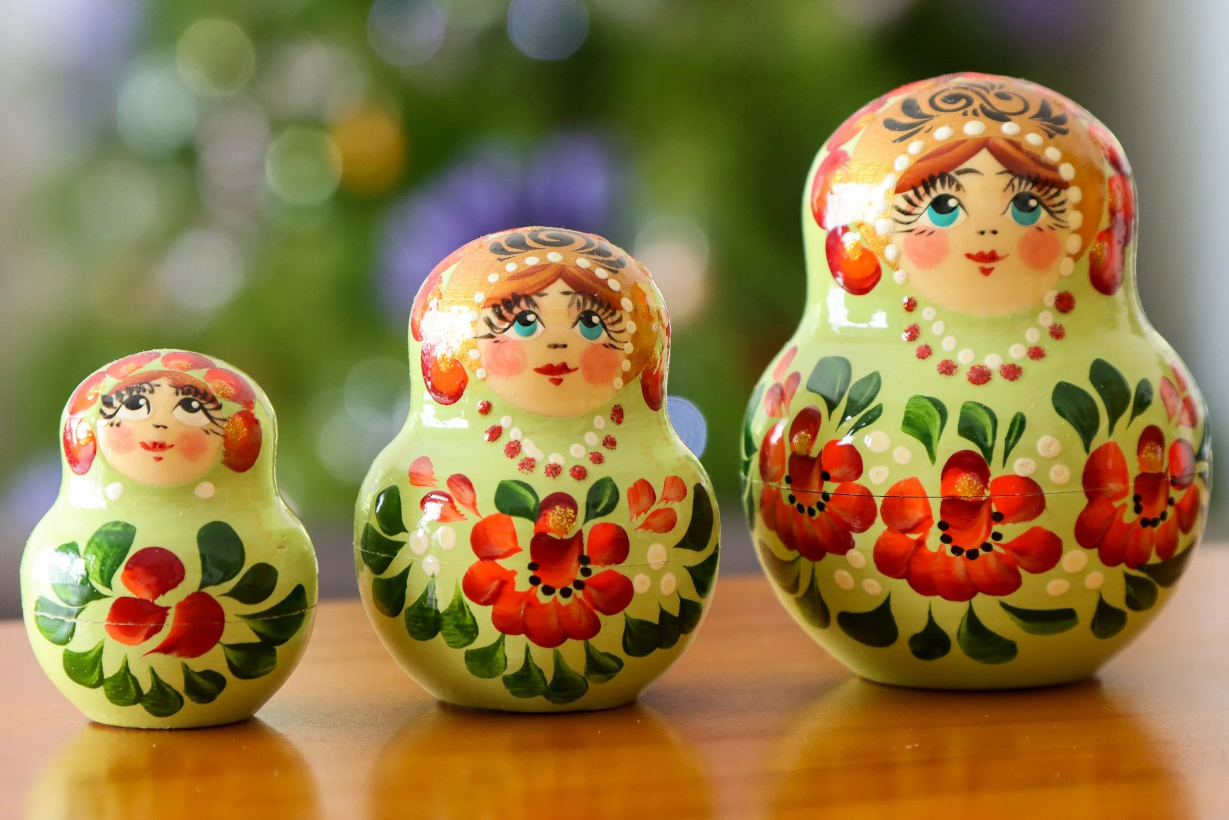 Four colorful Matryoshka dolls with floral designs on a wooden surface, with a blurred green background.