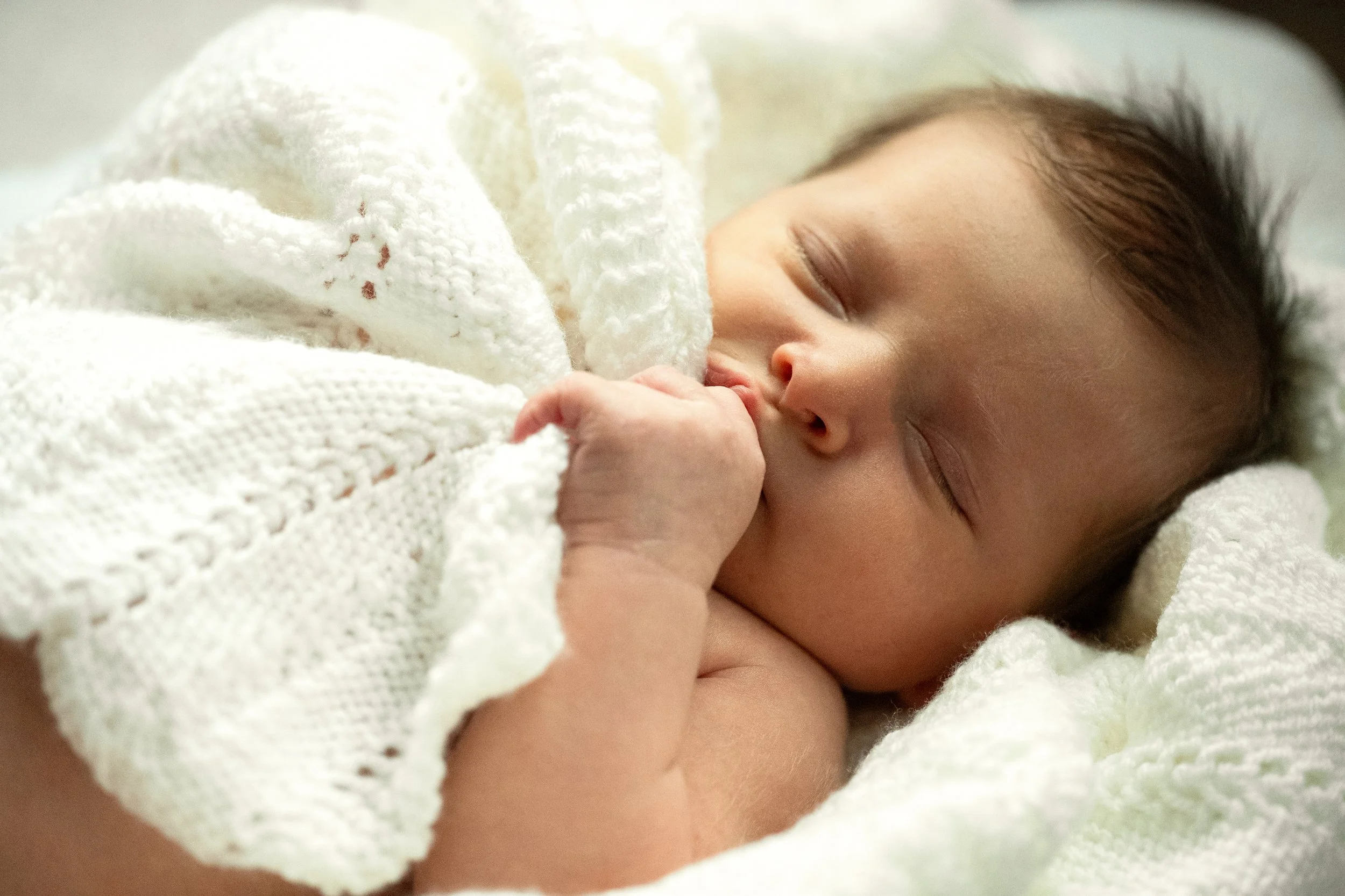 Sleeping newborn baby wrapped in blankets and sucking thumb