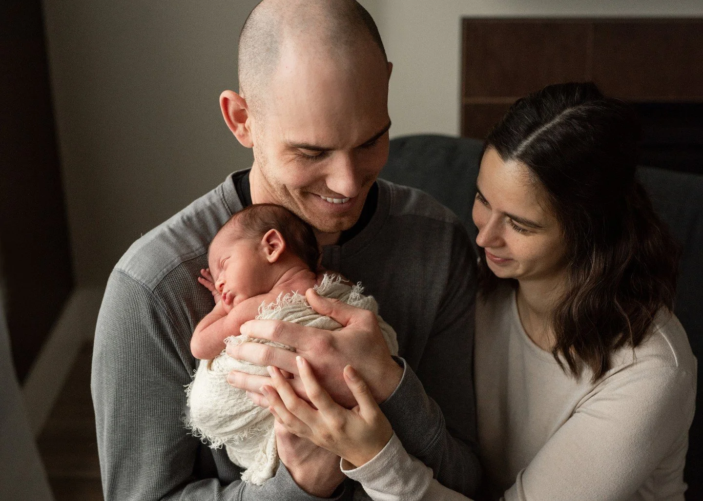 The simplicity of in-home newborn photography is what makes it so meaningful &mdash; capturing authentic emotion, quiet connection, and the feeling of these first days together. Like this beautiful moment between new parents and their tiny baby, wrap
