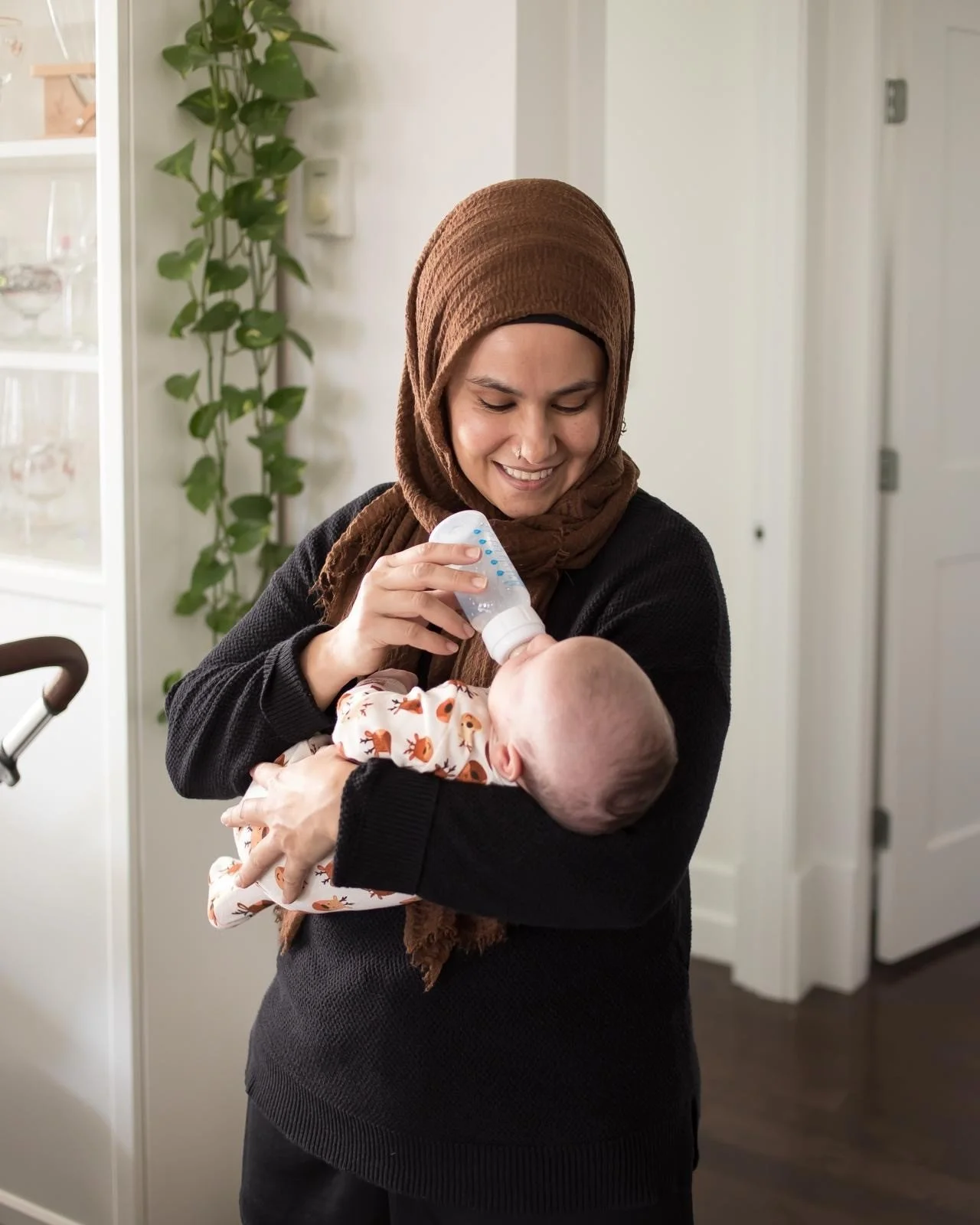 Newborn photographer feeding baby milk with baby bottle in between photos