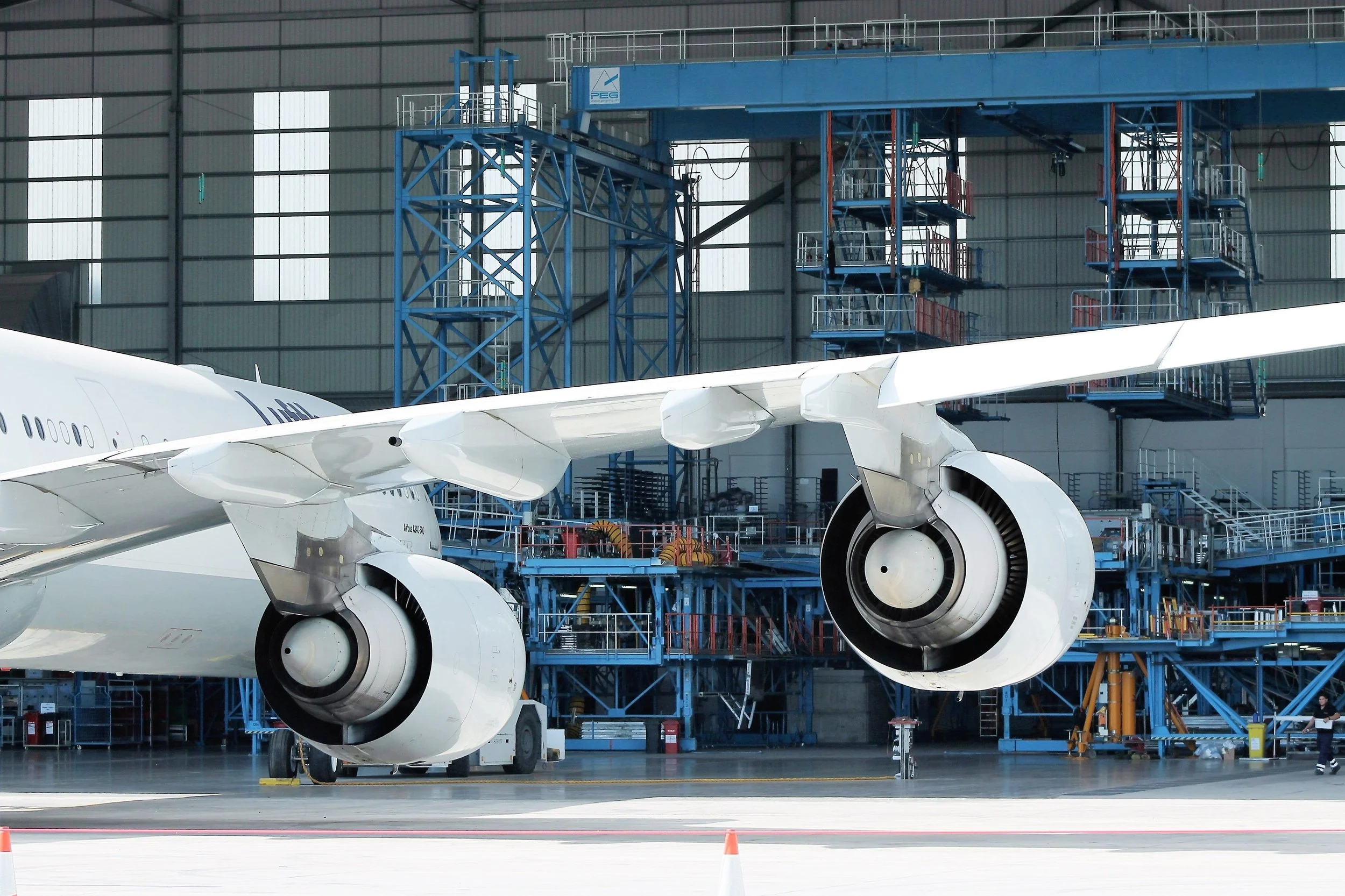 Widebody aircraft undergoing maintenance inside an aircraft hangar, showing engines, wing structure and MRO equipment.