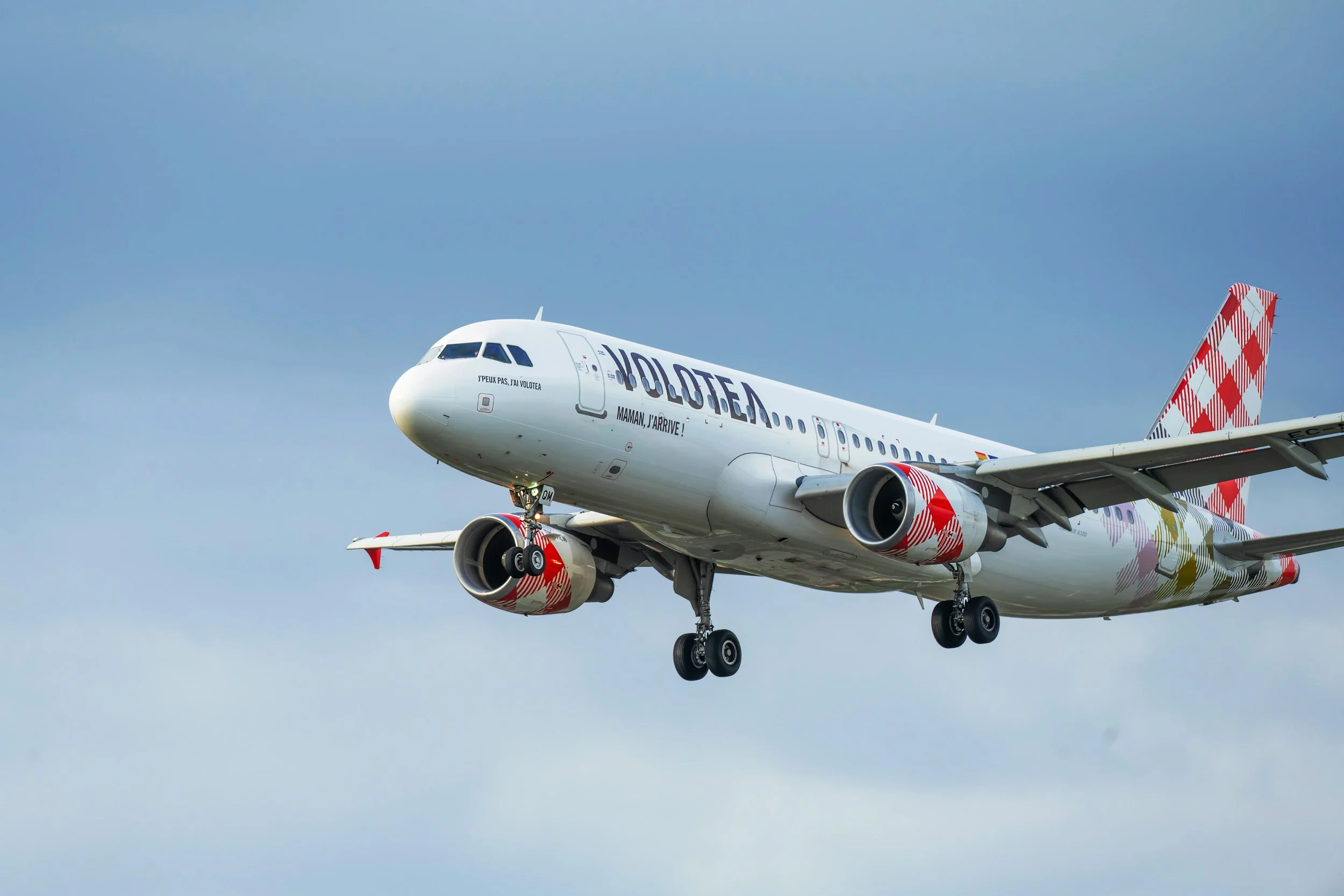 Volotea Airbus A319 aircraft approaching for landing against a cloudy blue sky, featuring the airline’s distinctive red-and-white tail design.