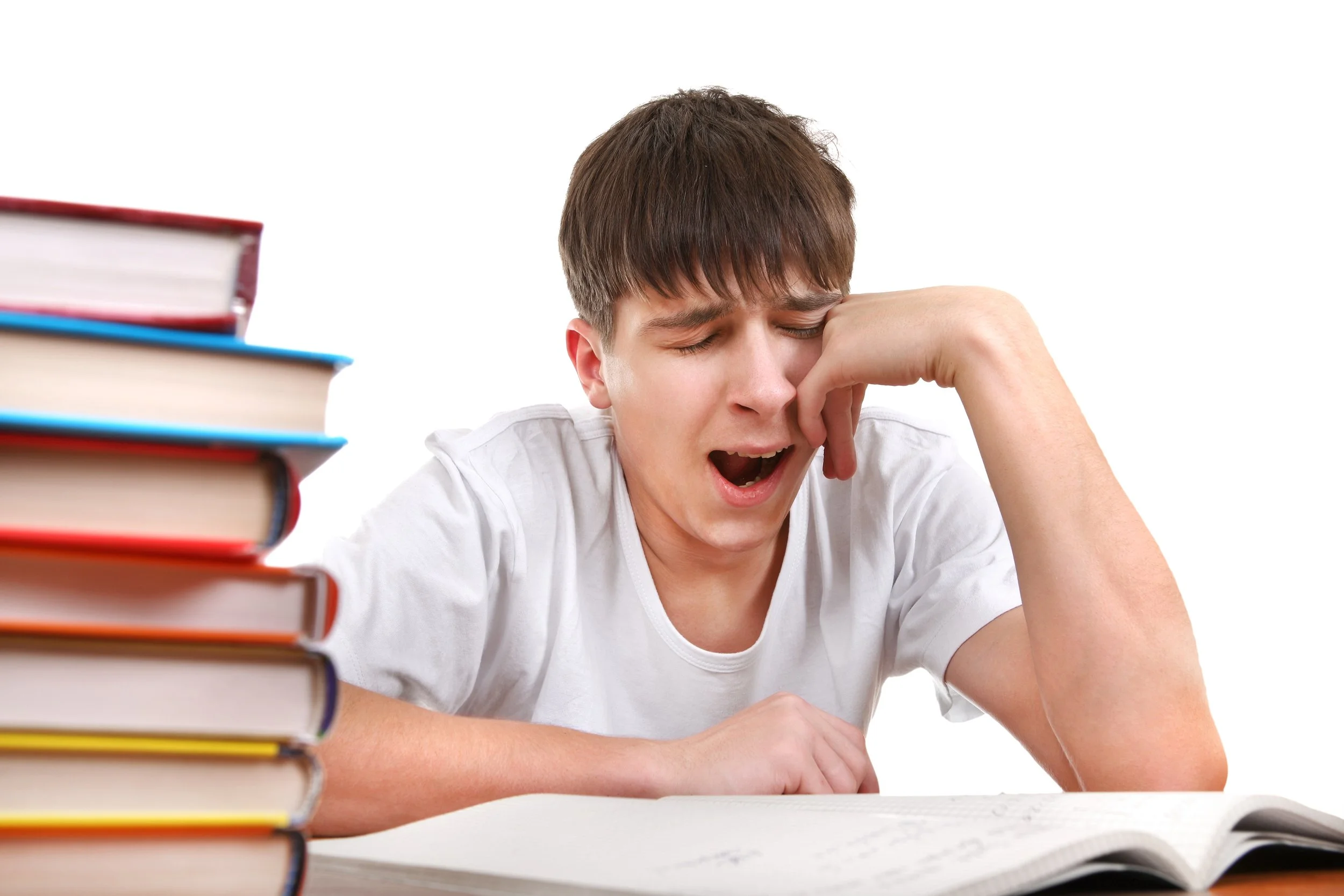 Teenage boy sat in class yawning next to pile of books