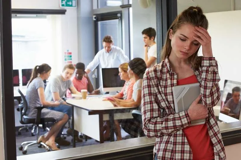 Teenage girl standing outside classroom excluded from classmates