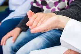 Two people holding hands on a white table, one wearing a black ring and the other wearing a silver ring.