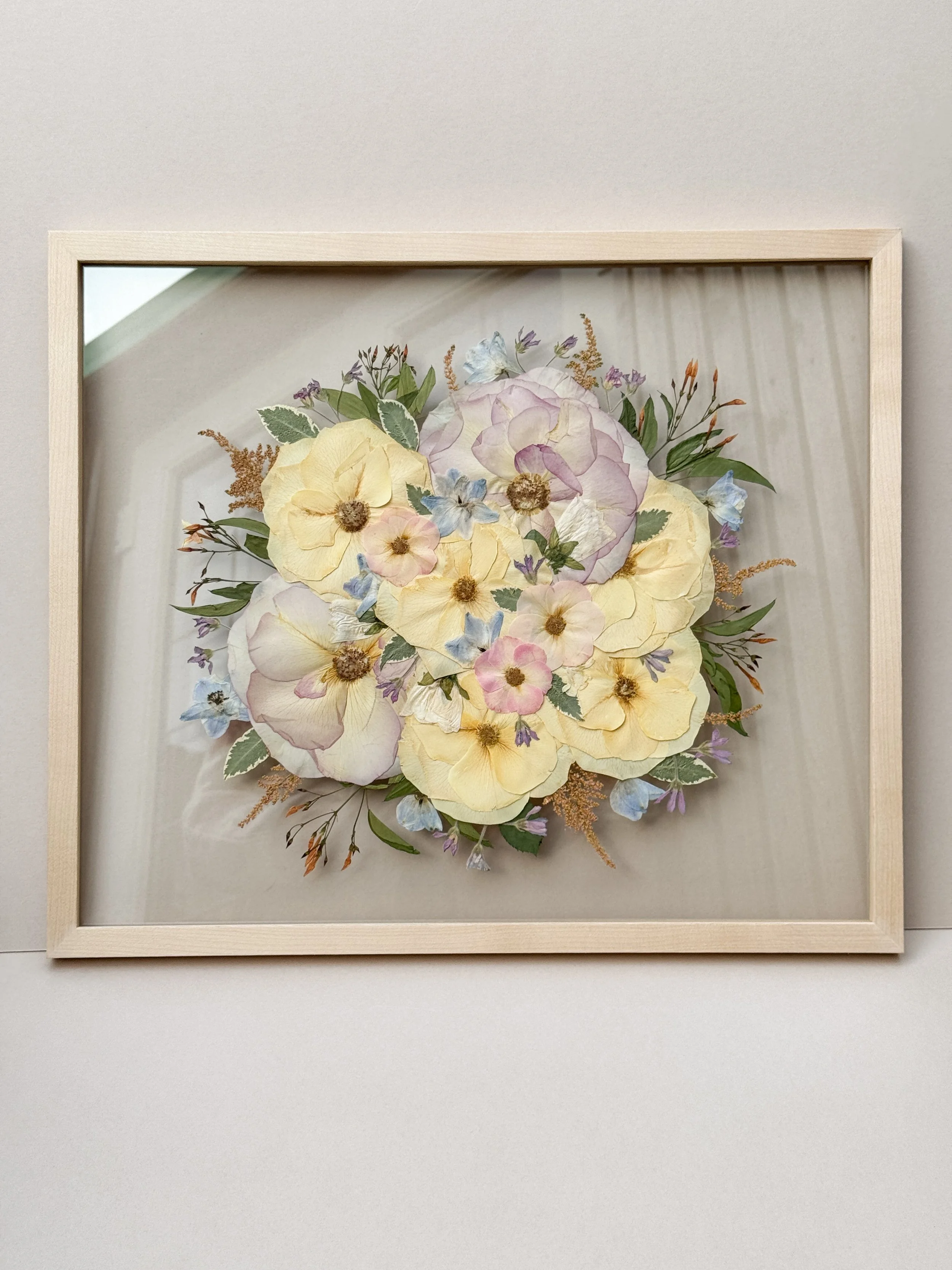 Framed pressed flower art with pastel-colored blooms and greenery.