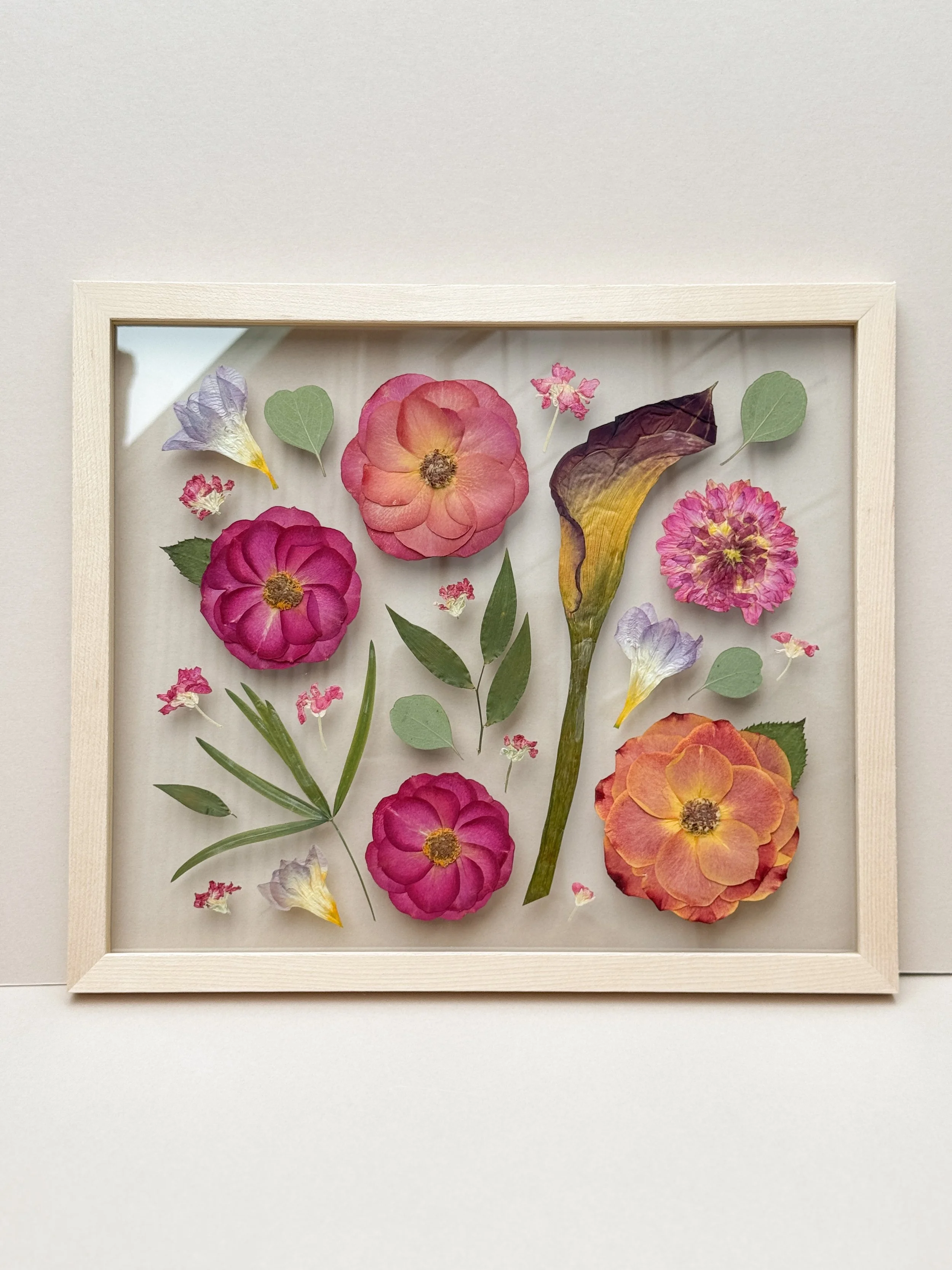 Pressed and dried colorful flowers, including pink, purple, and yellow flowers, arranged in a shadow box frame
