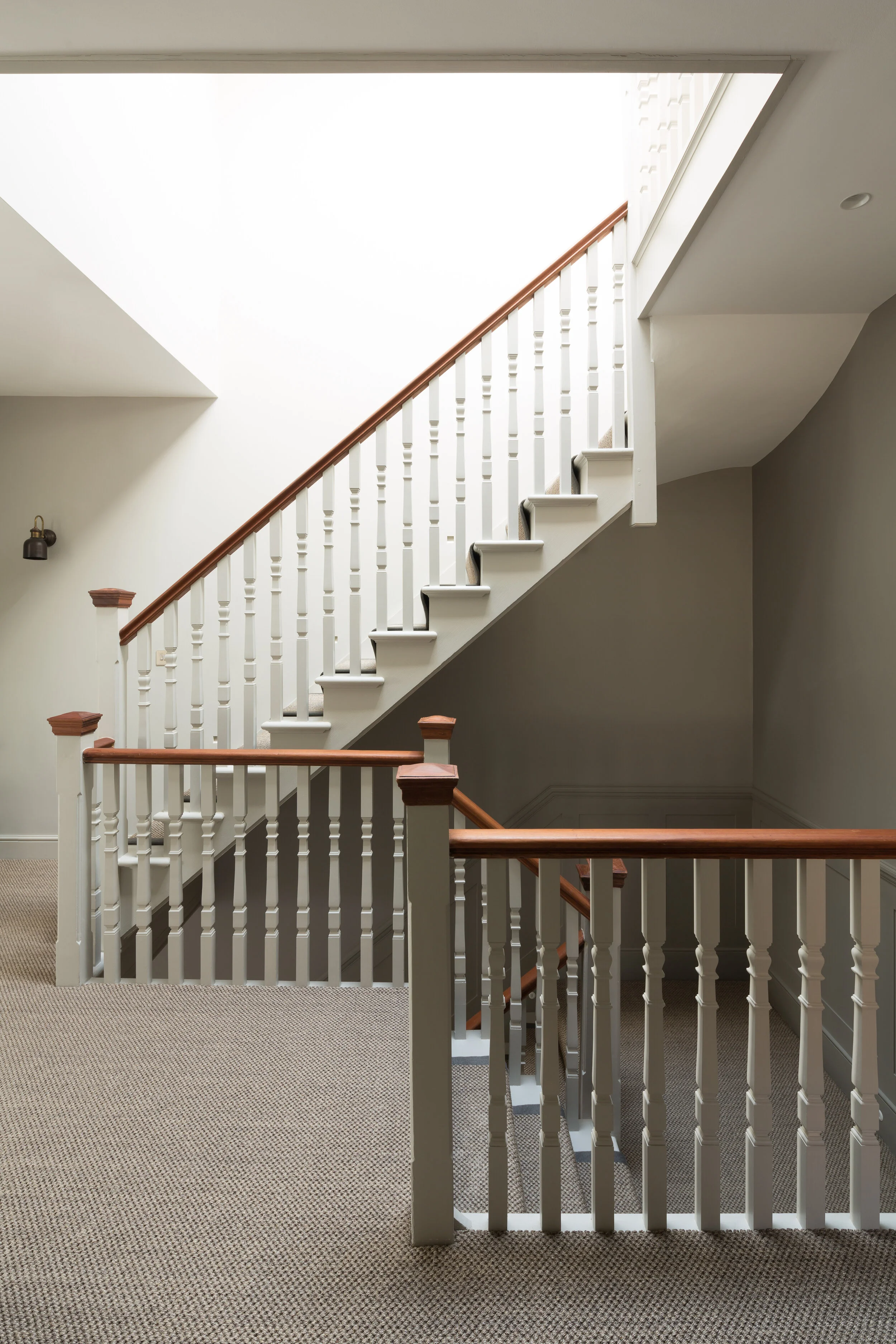 Interior view of a staircase with white spindles, wooden handrails, and beige carpet.