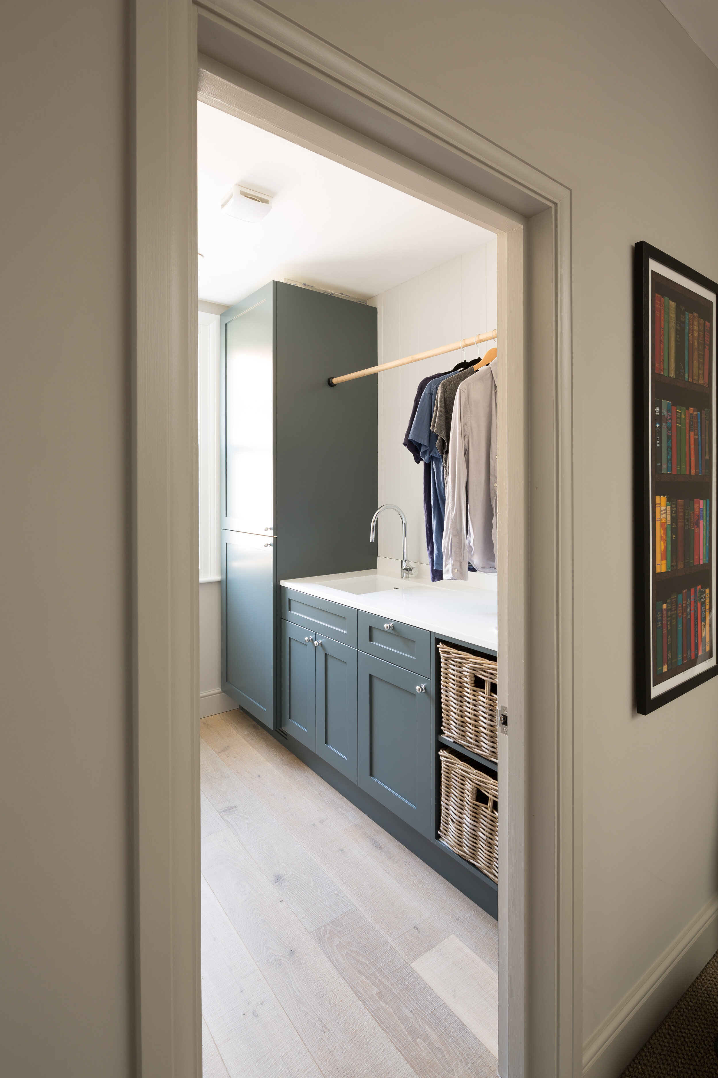 View of a laundry area with blue cabinets, a white countertop, a sink, and hanging clothes on a wooden rod.