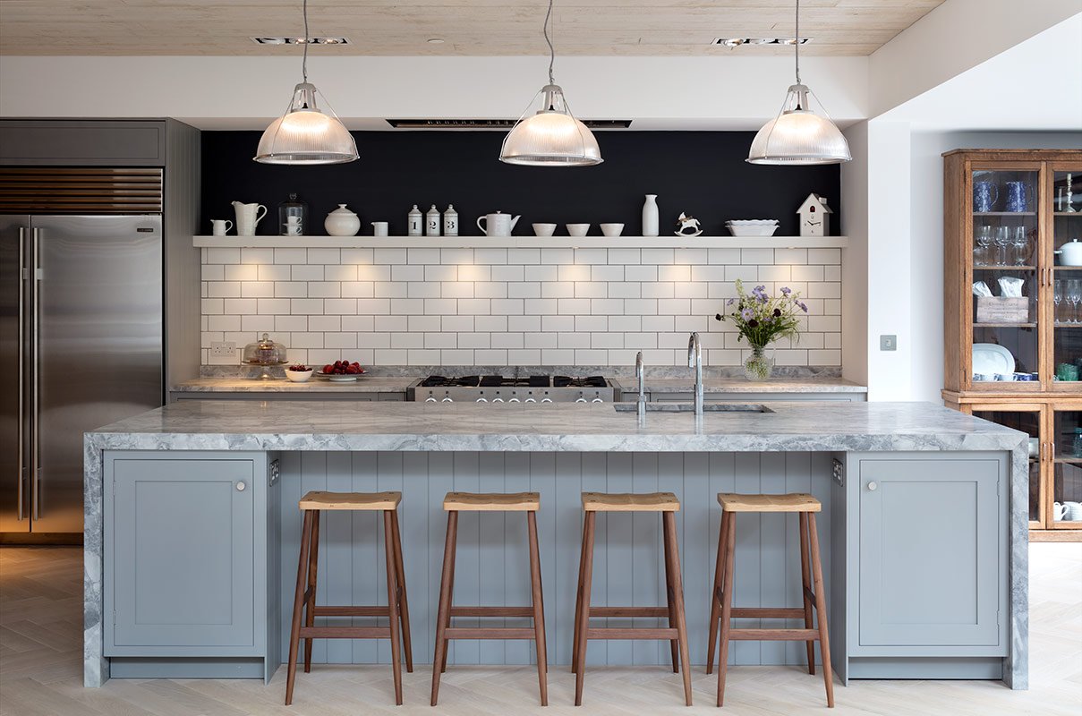 Modern kitchen with a marble island, four wooden bar stools, white subway tile backsplash, and overhead pendant lighting.