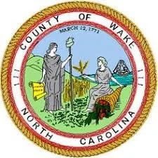 Seal of Wake County, North Carolina, with a woman and a man on a grassy landscape, one holding a staff, with a building and trees in the background.