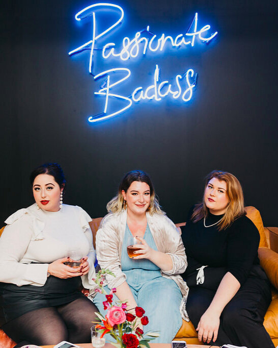 three women sitting on a couch under a neon sign