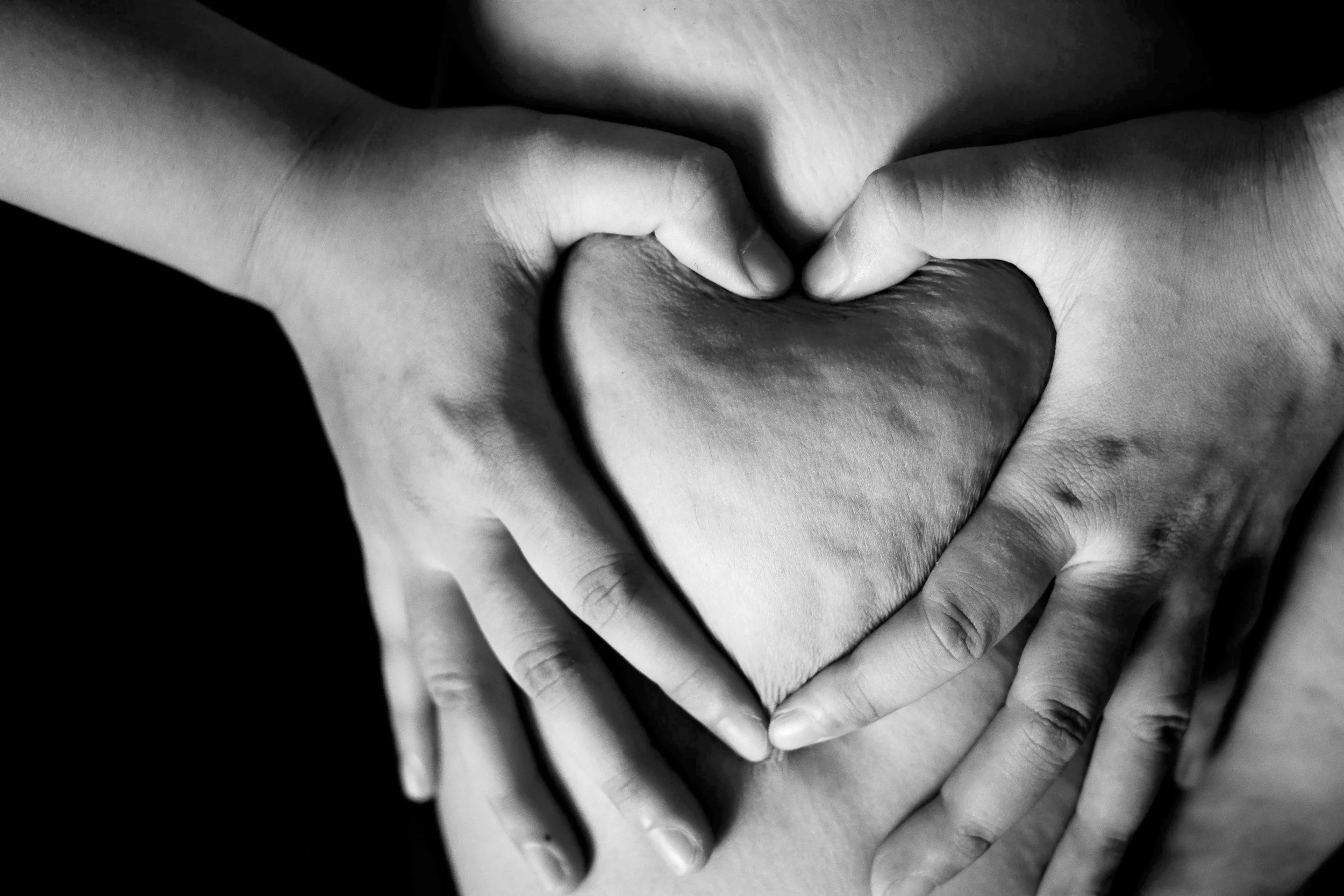 Two hands forming a heart shape around a person's chest, black and white photograph.